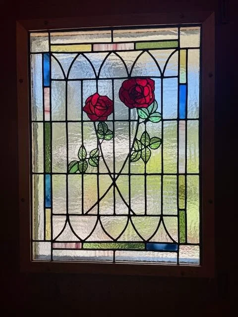 Stained glass window with two red roses and green leaves, framed by geometric colorful glass panels.