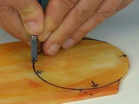 person cutting a circle from orange and yellow opalescent stained glass with a hand tool