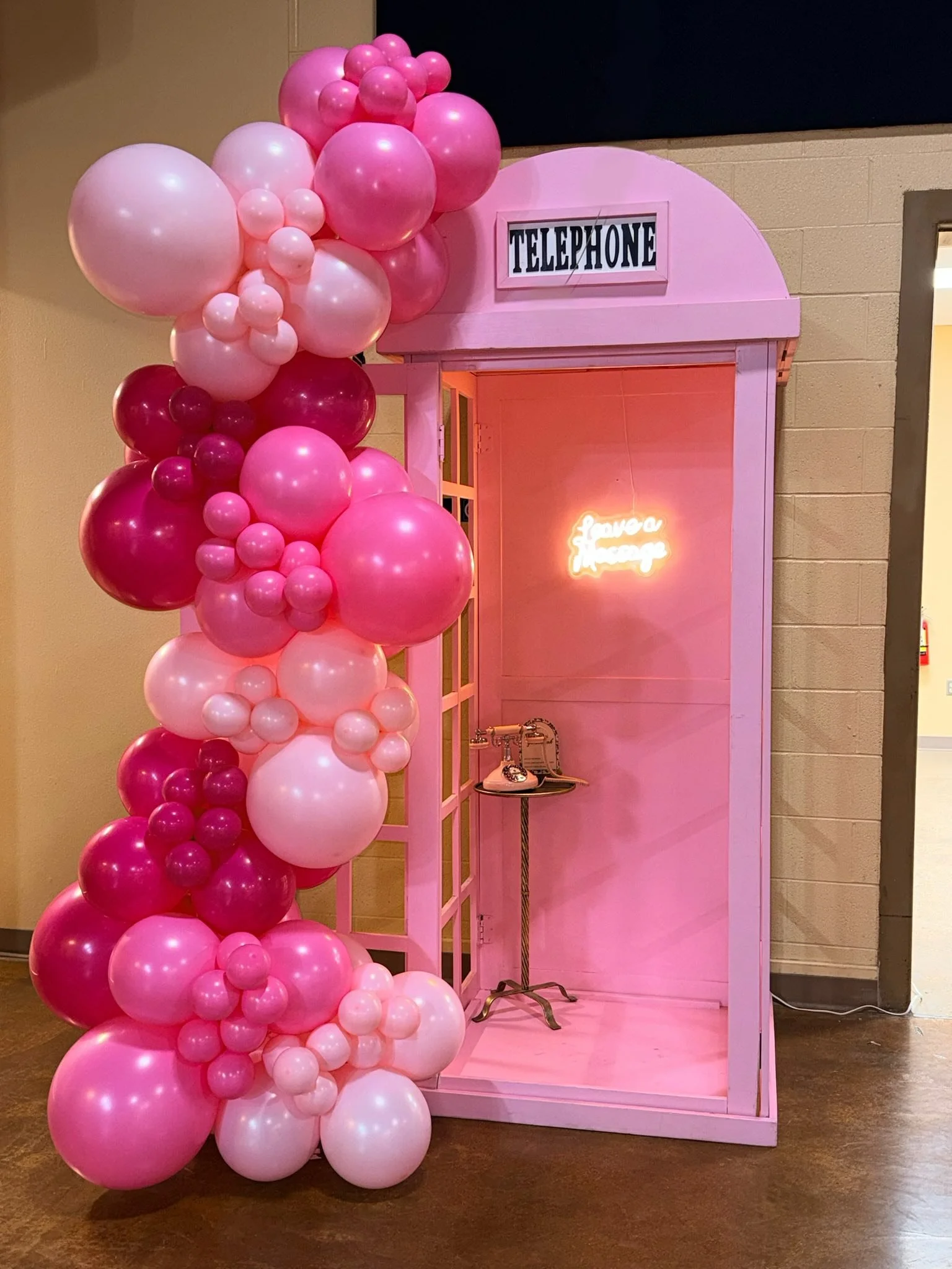 Pink telephone booth with open door, inside an illuminated sign says "leave a message," and a tall decorative column