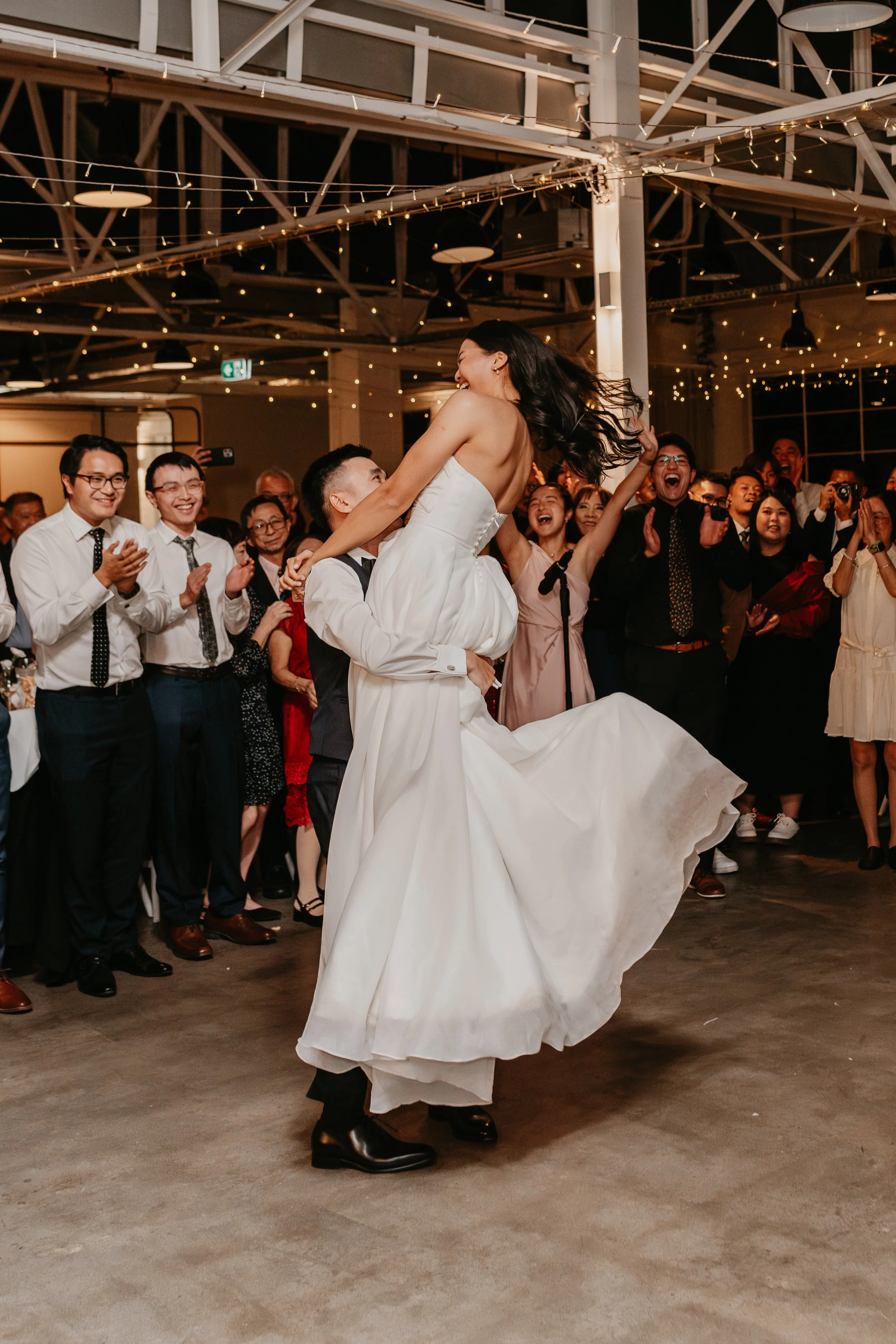 A couple dancing happily, man in a white shirt and green pants, woman in a white dress with flowers in her hair.