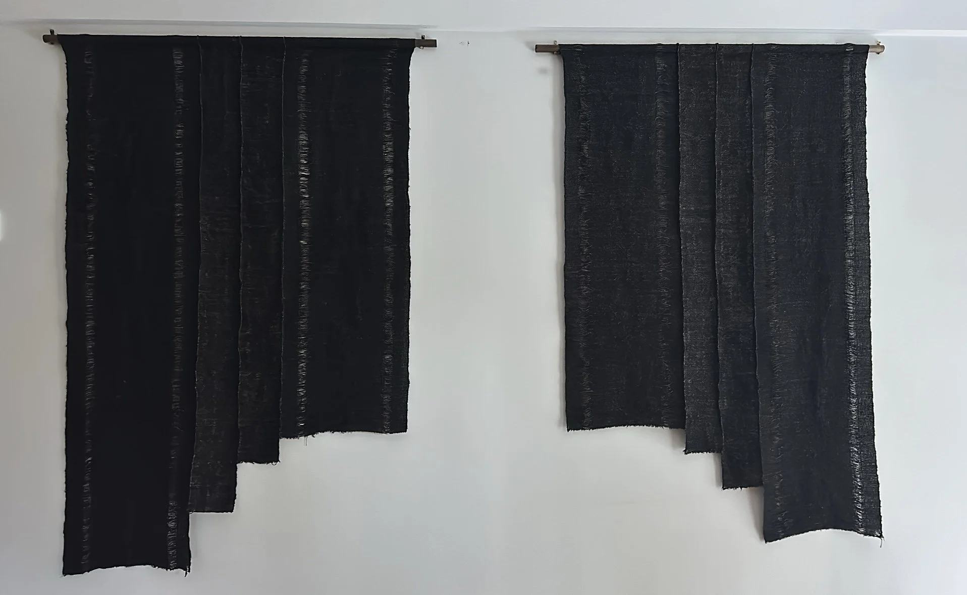 Two hand woven black fabric panels hanging on a white wall