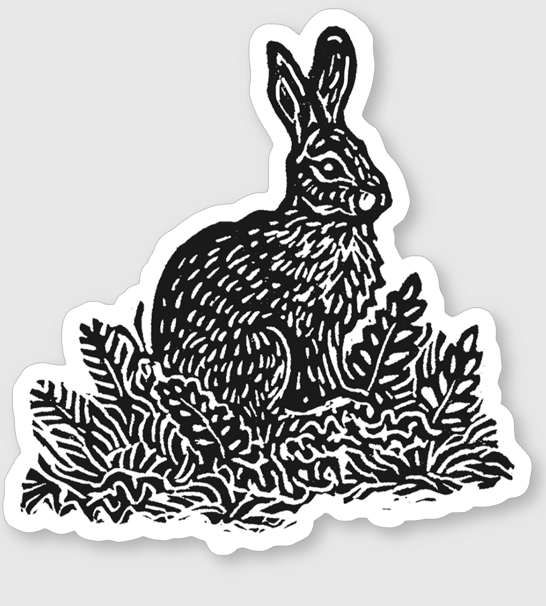 Black and white sticker of a rabbit sitting among plants and foliage.