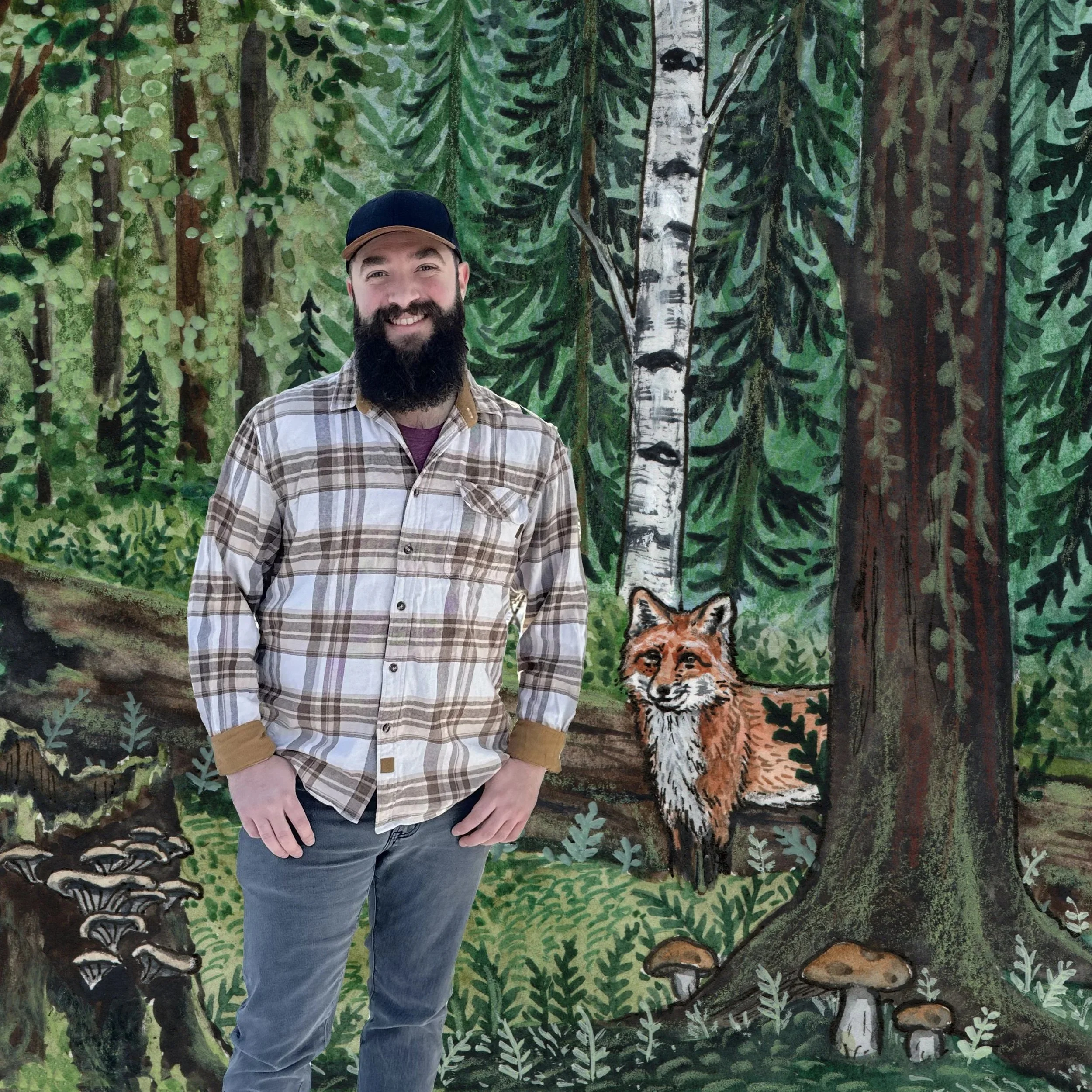 A man with a beard smiling, wearing a plaid shirt, gray pants, and a black cap, standing in front of a painted mural of a forest scene with trees, mushrooms, and a fox.
