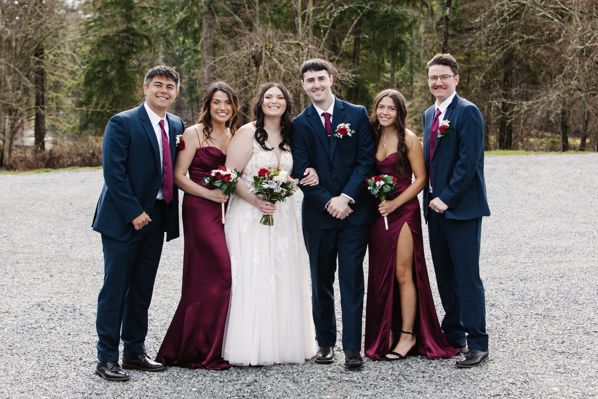 Group of six young people dressed in formal attire outdoors, smiling at the camera, with trees in the background.