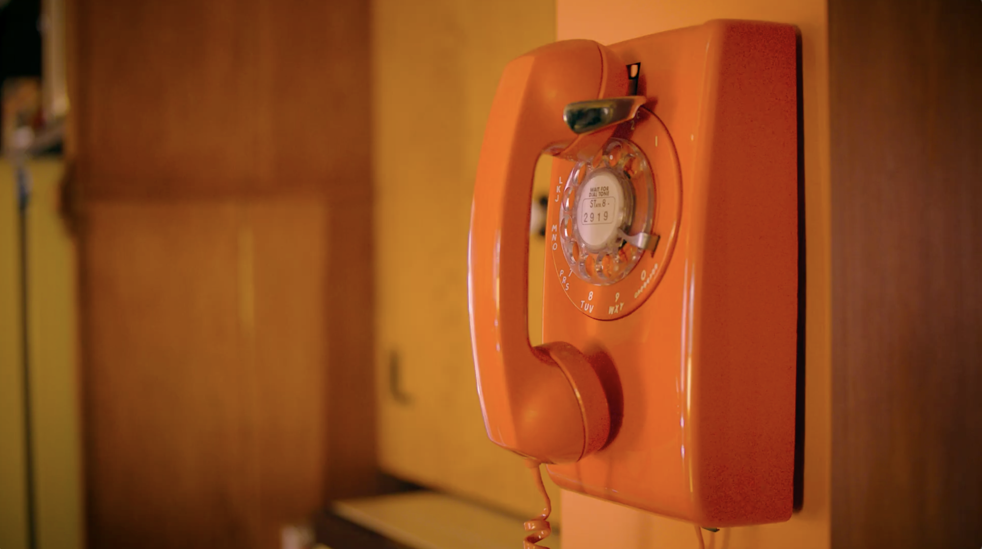 A vintage orange rotary telephone with a circular dial resting on a wooden surface.
