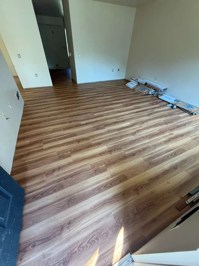 Empty room with newly installed wood laminate flooring, some newspapers on the floor near the wall, and interior doorways visible.