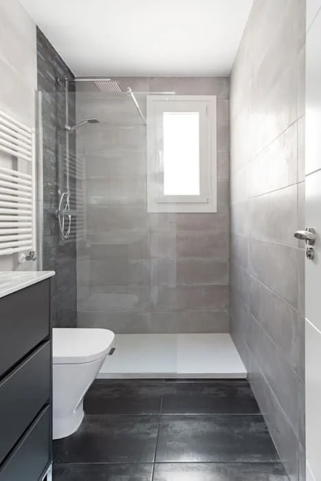 Modern bathroom with gray tiled walls, a window, a walk-in shower with a rainfall showerhead, and a white toilet.