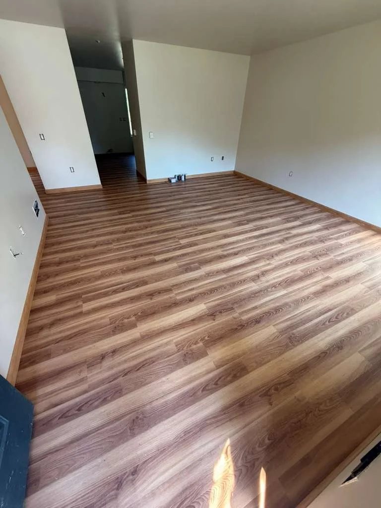 Empty room with newly installed wood flooring, white walls, and a doorway leading to another room.