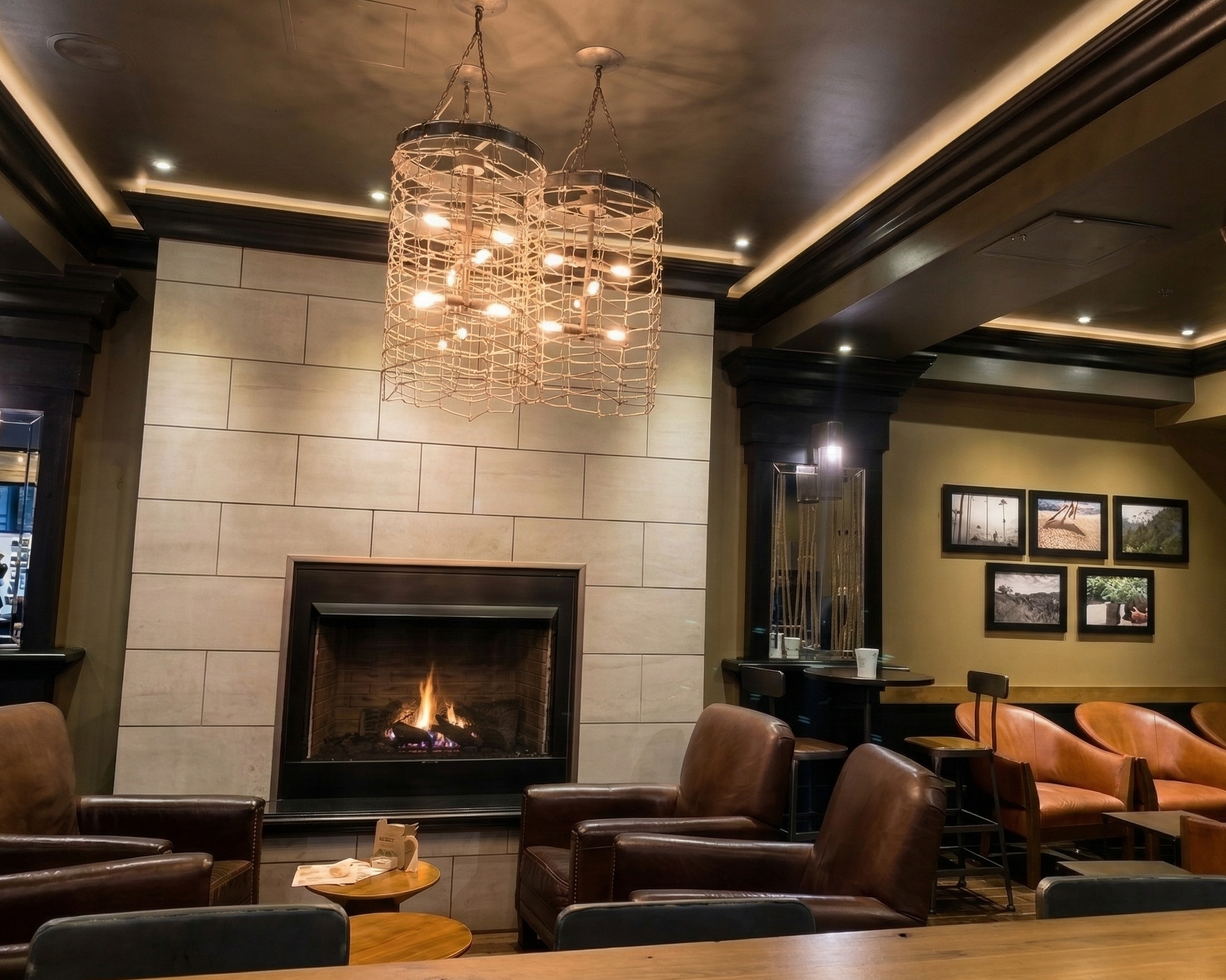 Cozy lounge area with a lit fireplace, leather armchairs, and framed photographs on the wall, illuminated by warm lighting.