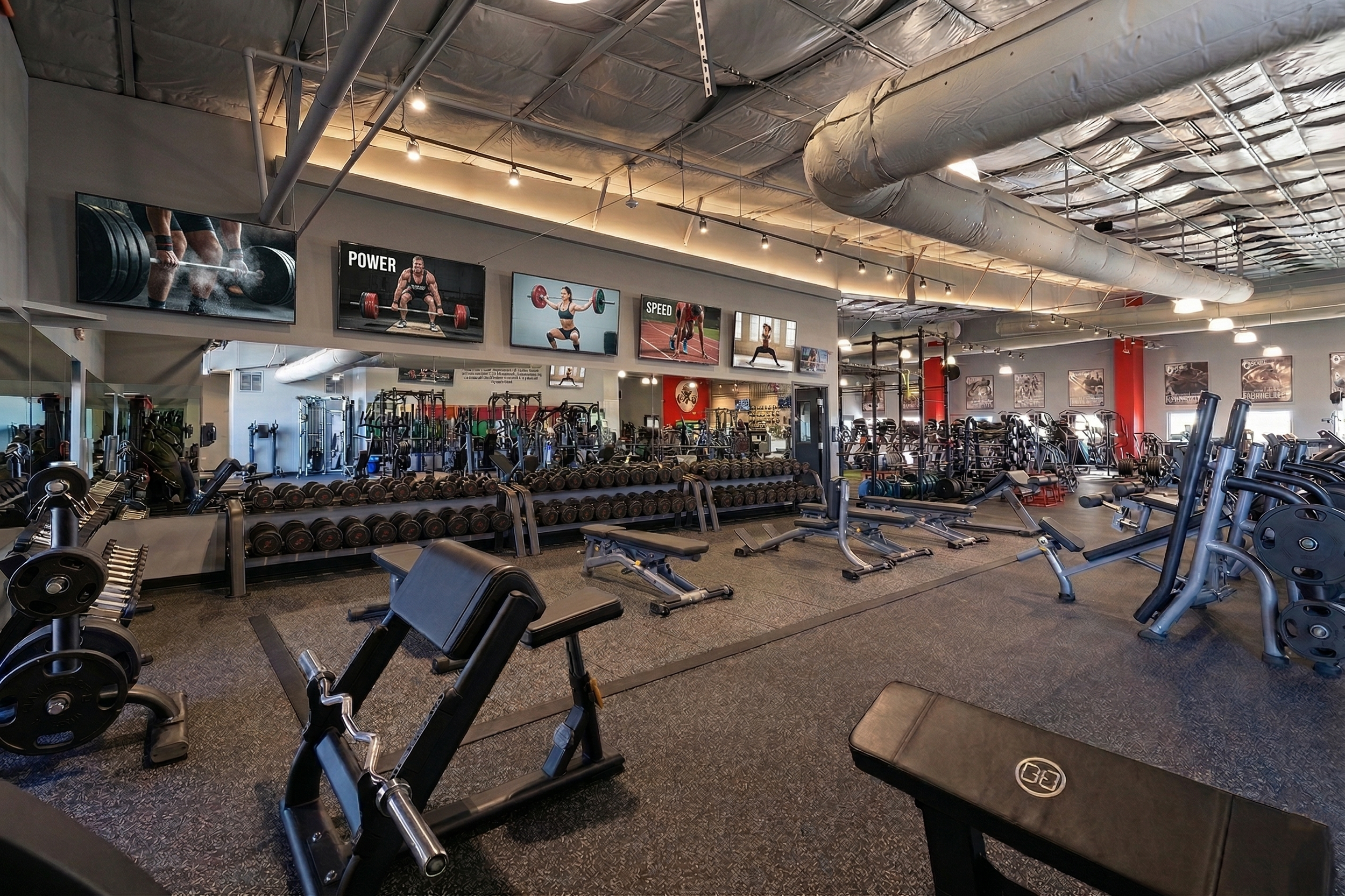 Interior of a gym with various weightlifting and exercise equipment, mirrors, and motivational posters on the wall.