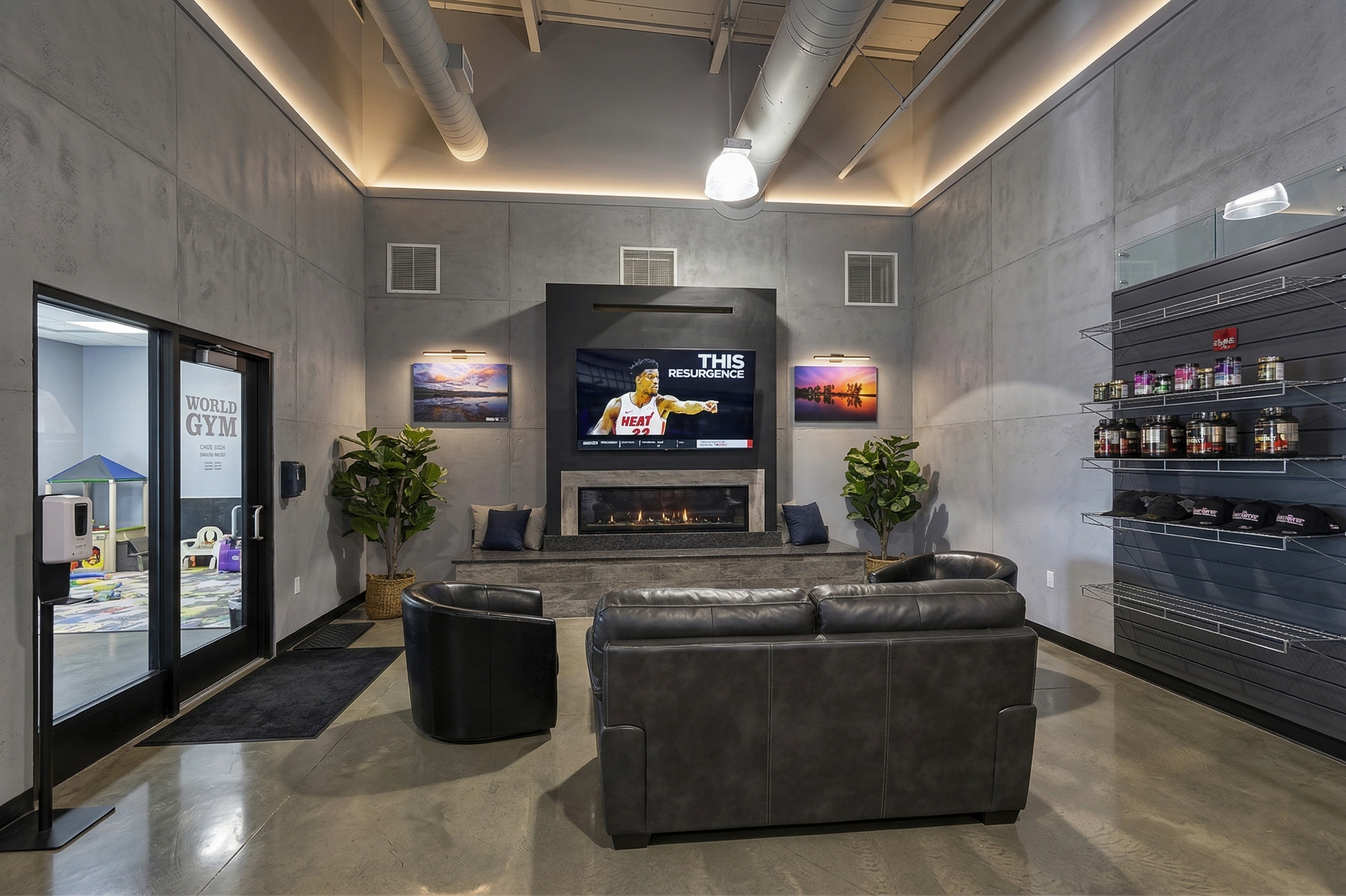Modern lounge area with leather sofa, two armchairs, and a fireplace, featuring a flat screen TV on a gray wall, with framed sunset paintings, potted plants, and a view of a children's playroom through sliding glass doors.