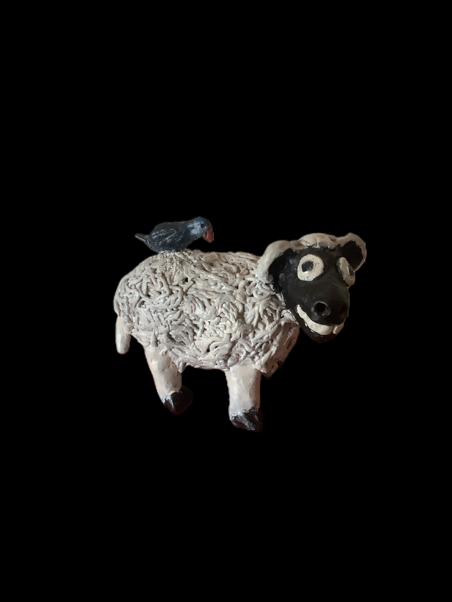 Artistic sculpture of a sheep with a textured body, a black face, and brown hooves, with a small bird perched on its back, set against a black background.  Also known as Shorn the Terrible