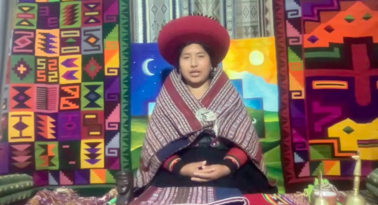 Person wearing traditional clothing with geometric patterns and colorful textiles in the background.