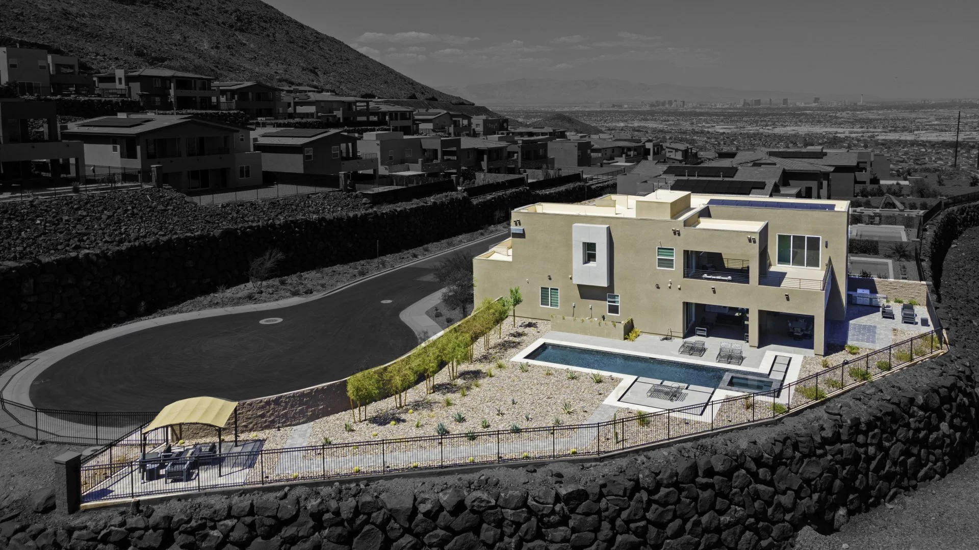 Modern house with pool on hillside, surrounded by desert landscape and city view in background.