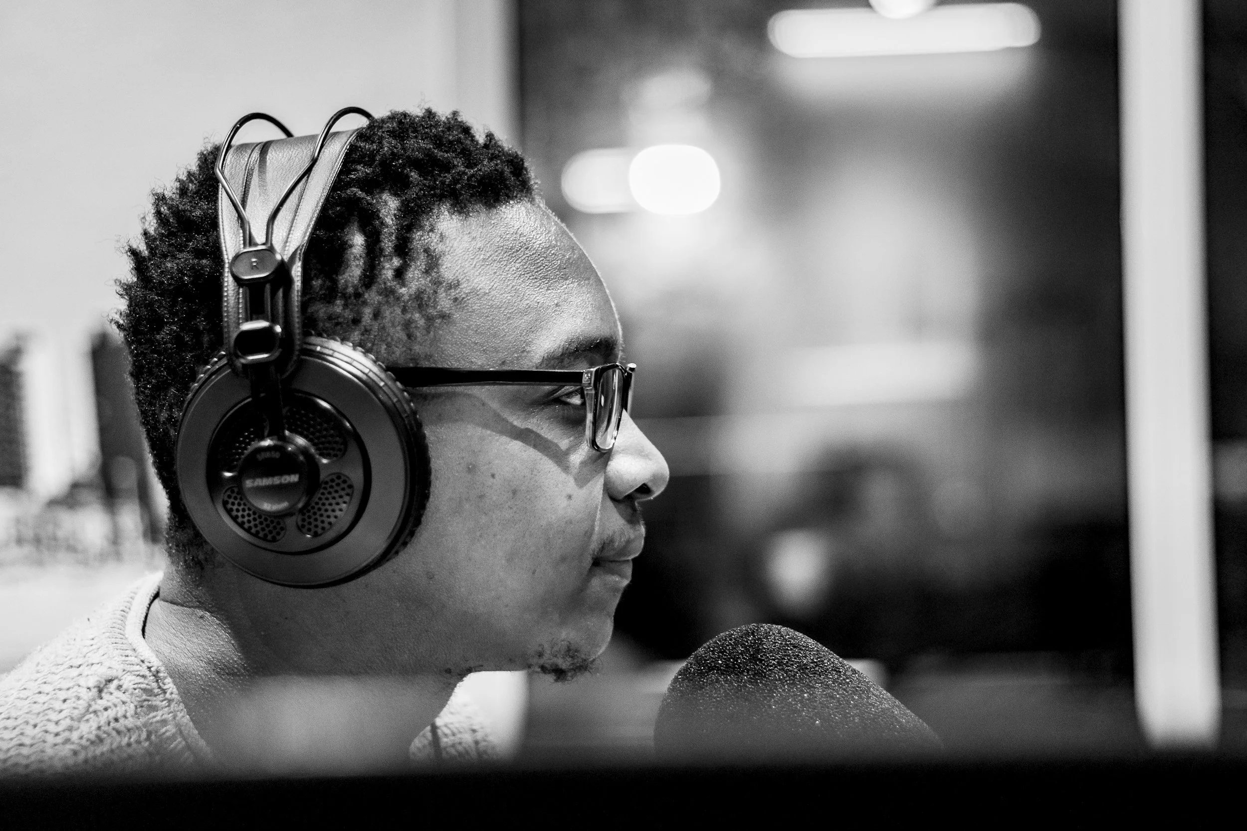 Black and white photo of a man with glasses wearing headphones, speaking into a microphone.