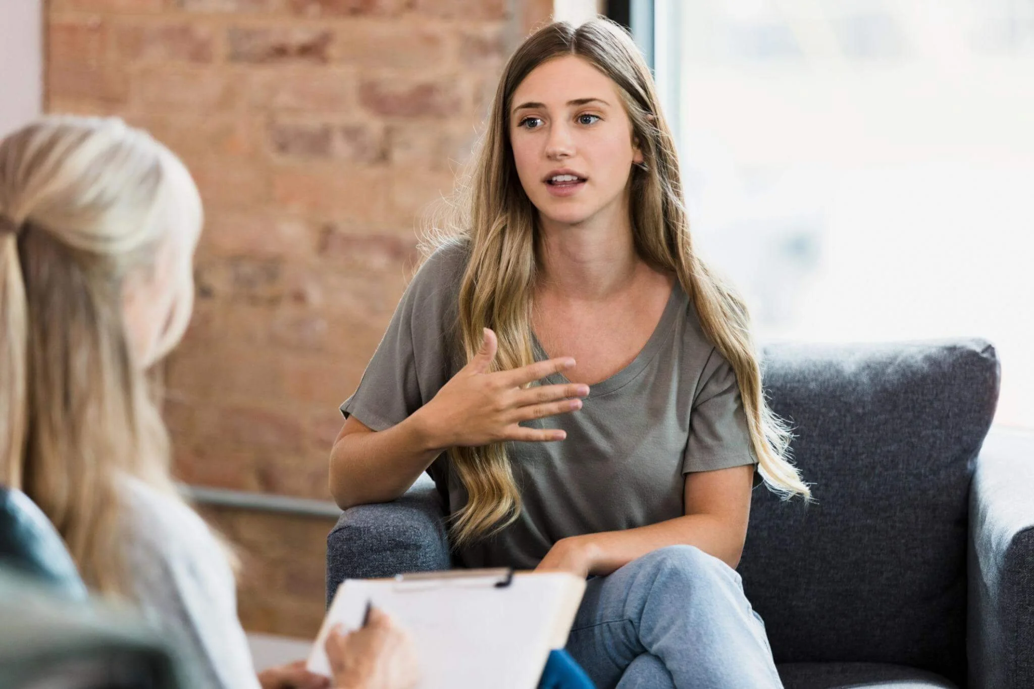 Two women having a conversation in a cozy, modern office or living room, one woman is speaking while the other listens and takes notes.