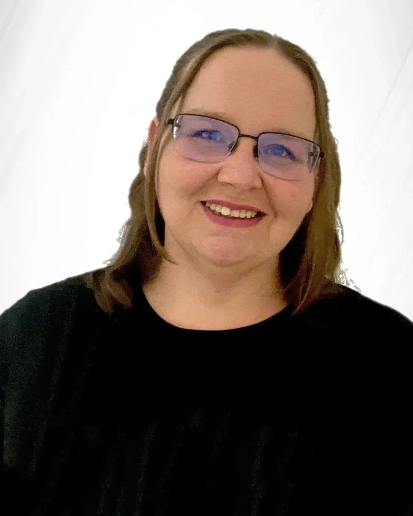A woman smiling, wearing glasses and a black top, standing in front of a plain white wall.