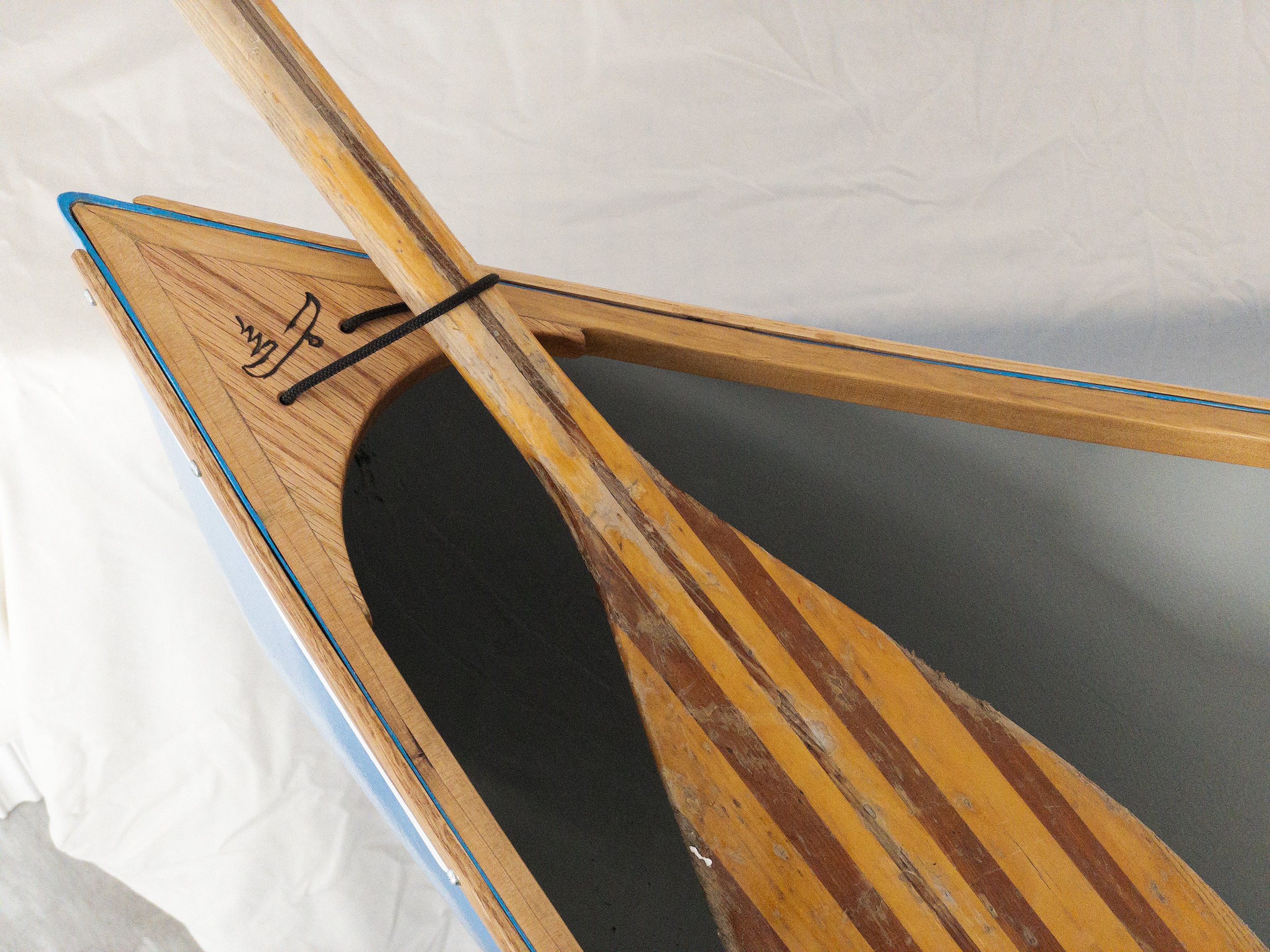 Wooden canoe paddle resting on a wooden canoe deck with engraved symbol.