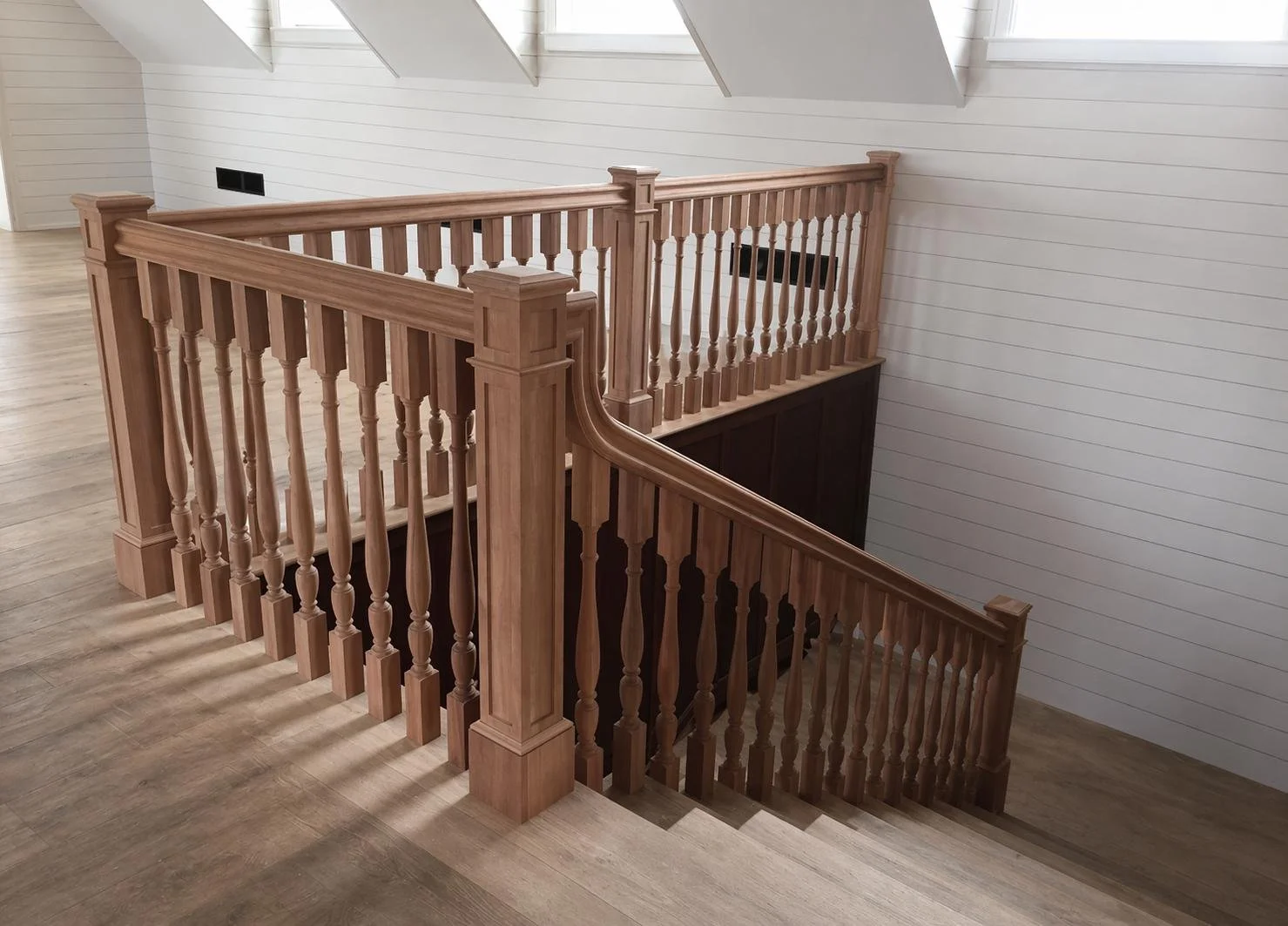 Wooden staircase banister with turned spindles and newel posts in a bright, modern interior with white shiplap walls and skylight windows.