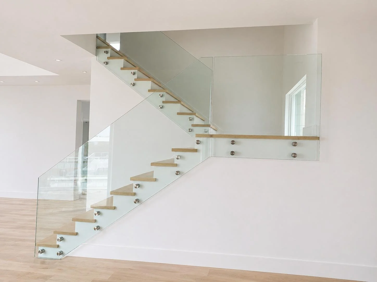 Modern staircase with glass sides and wooden steps in a bright, minimalistic interior.