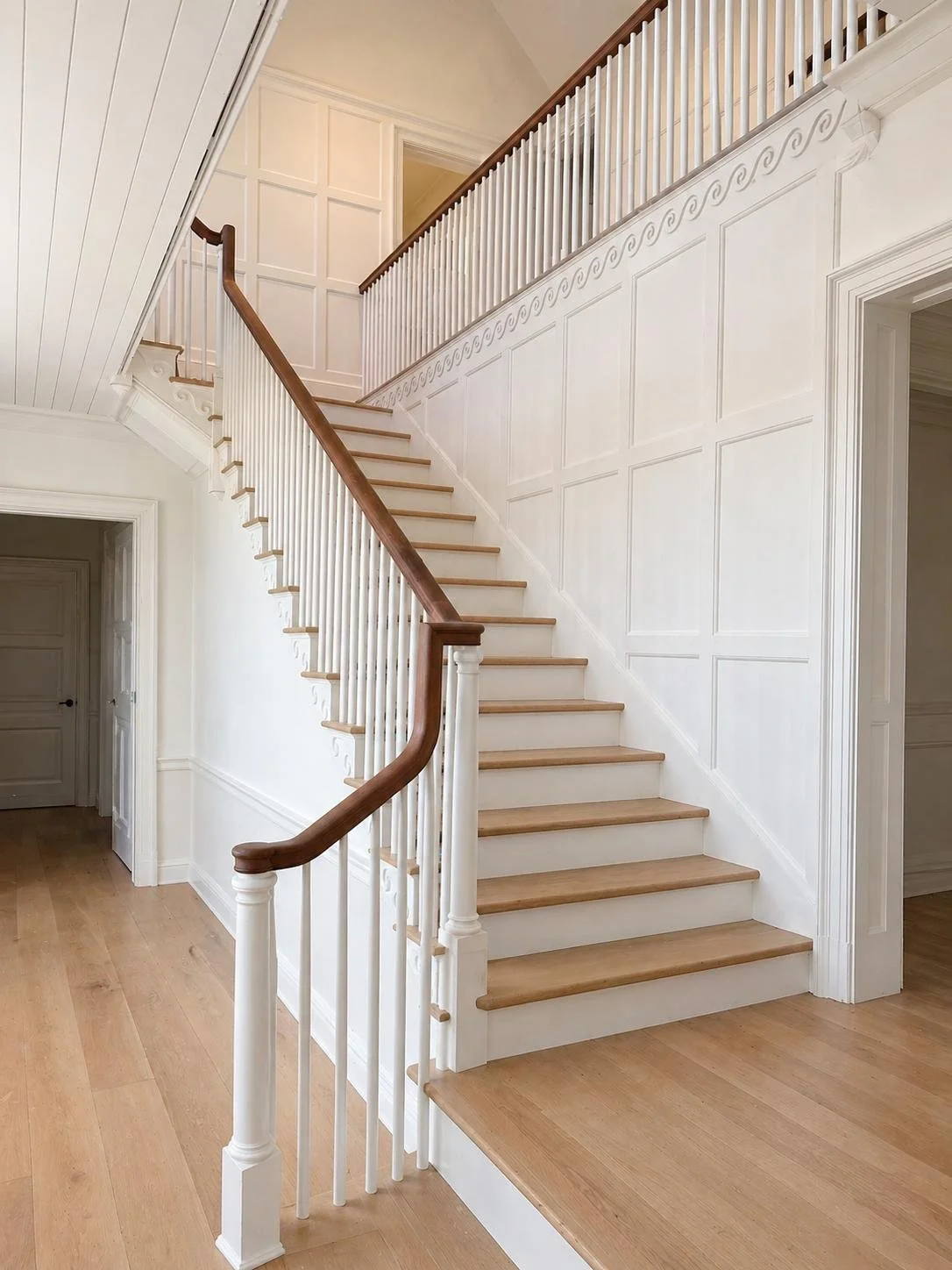 Interior view of a wooden staircase with white balusters and a wooden handrail in a home with beige walls and hardwood flooring.