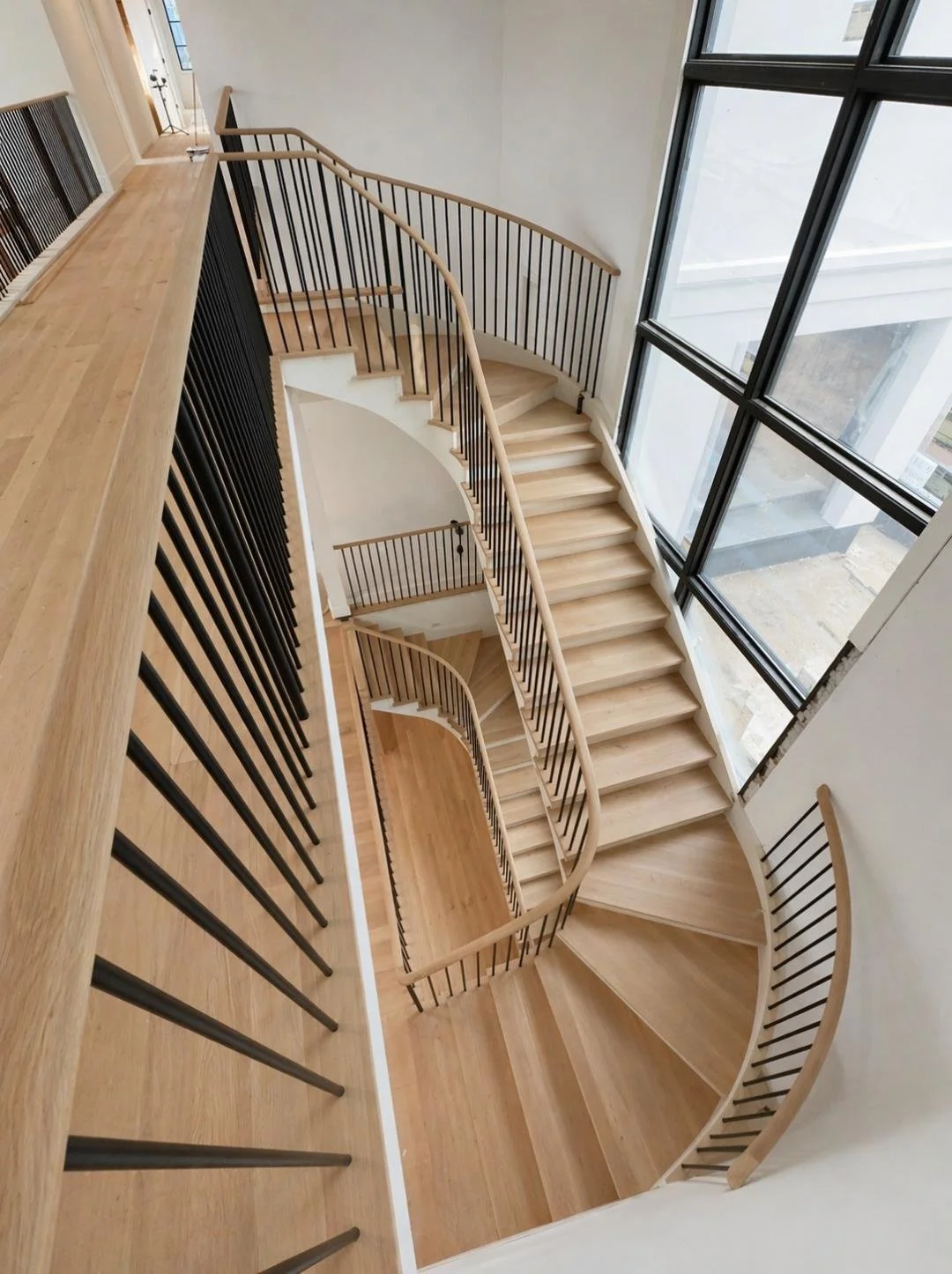 Interior view of a modern wooden staircase with metal handrails, positioned next to large floor-to-ceiling windows.