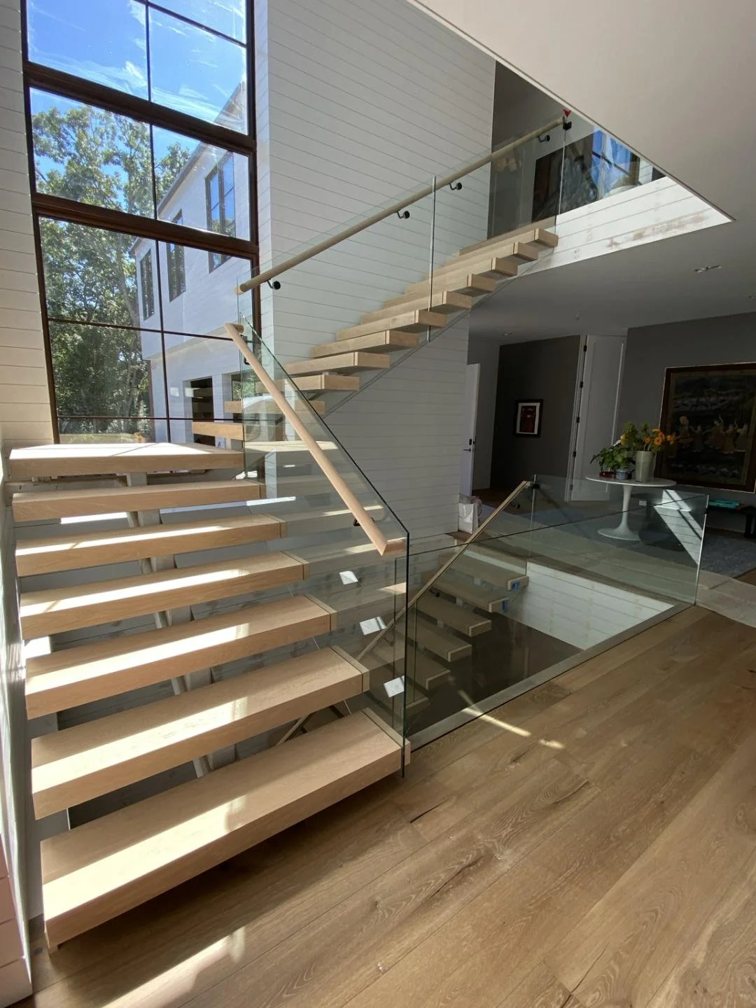 Modern interior staircase with wooden steps, glass panels, and metal supports in a well-lit room.