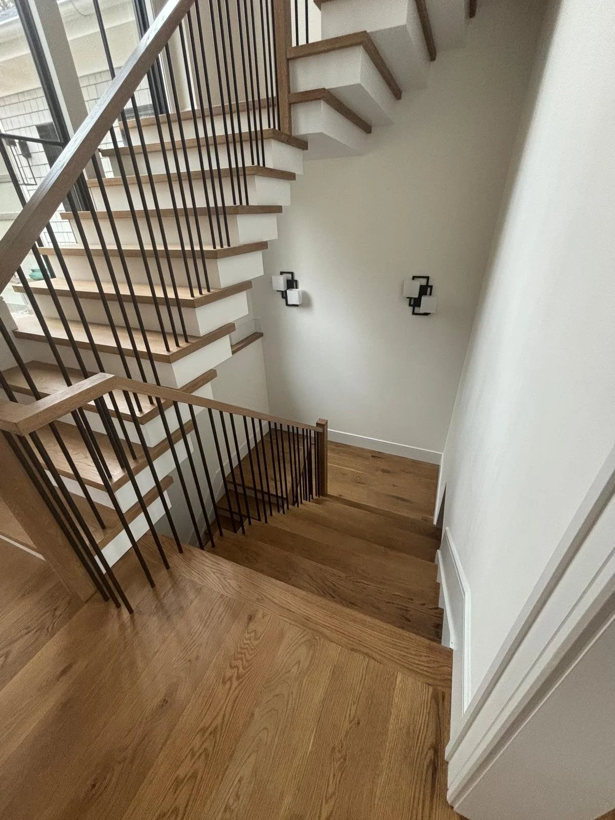 View of a staircase with wooden steps and black metal railings, white walls, and wall-mounted light fixtures in a modern interior.