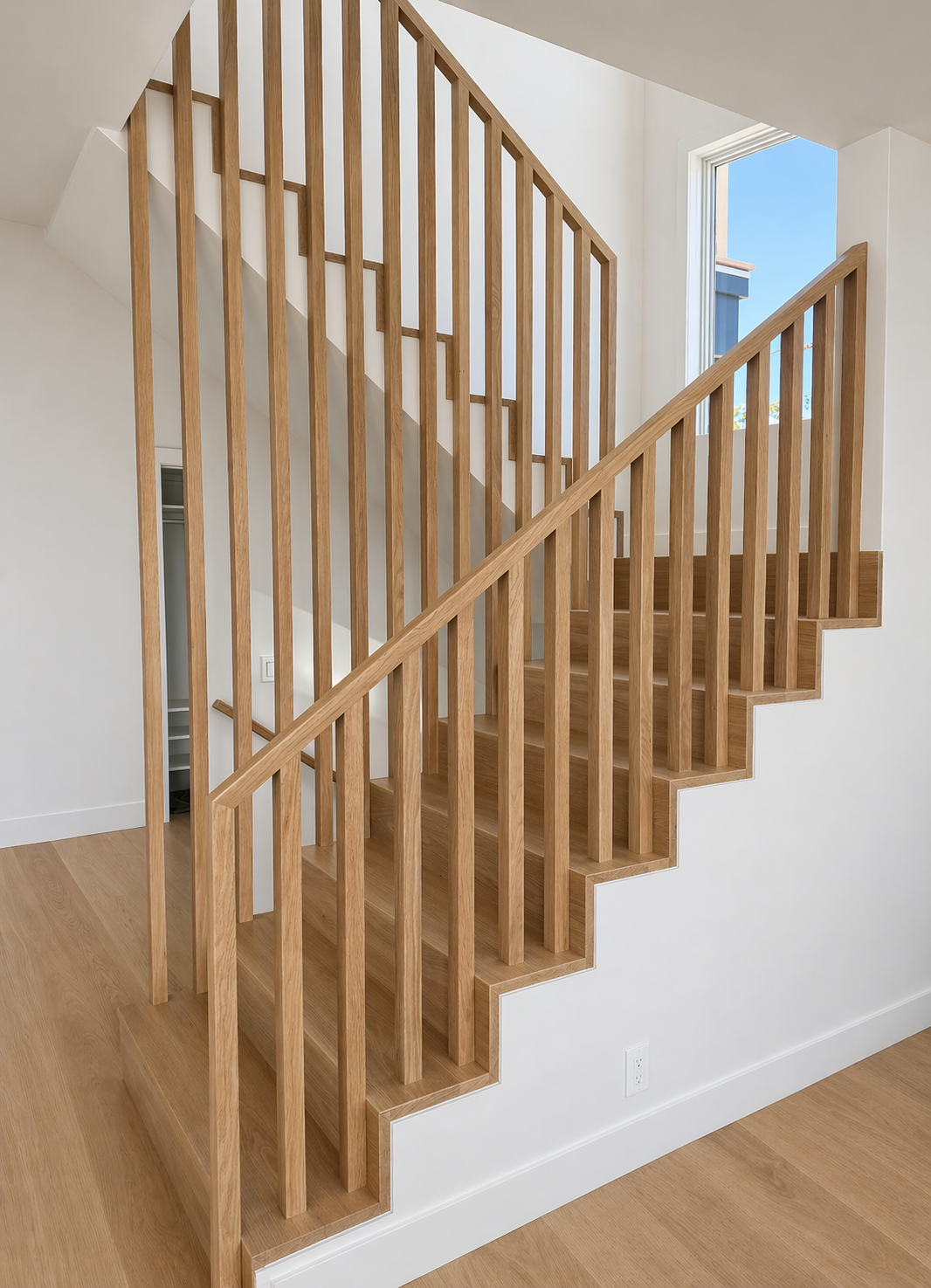 Wooden staircase with vertical slat railing and a large window at the top, letting in natural light.