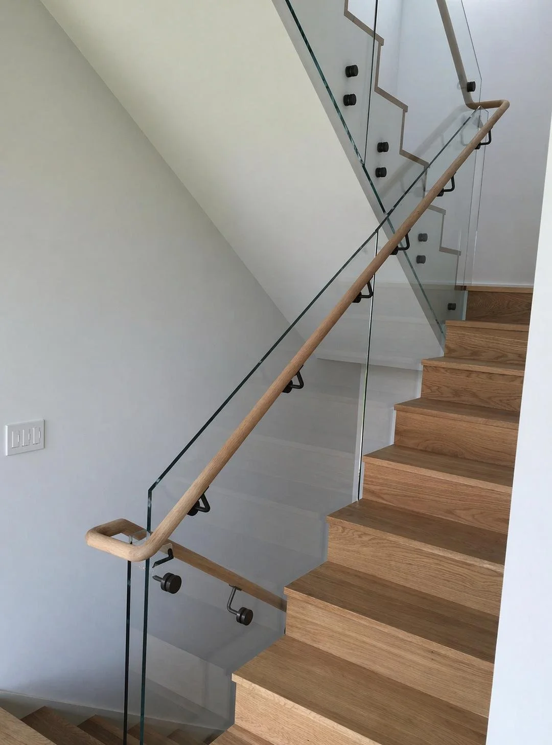 Modern staircase with wooden steps, glass and metal railing, and a wooden handrail.
