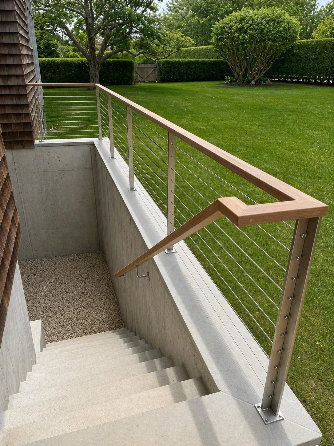View of outdoor stairs leading down to a grassy backyard with trees and a wooden fence.