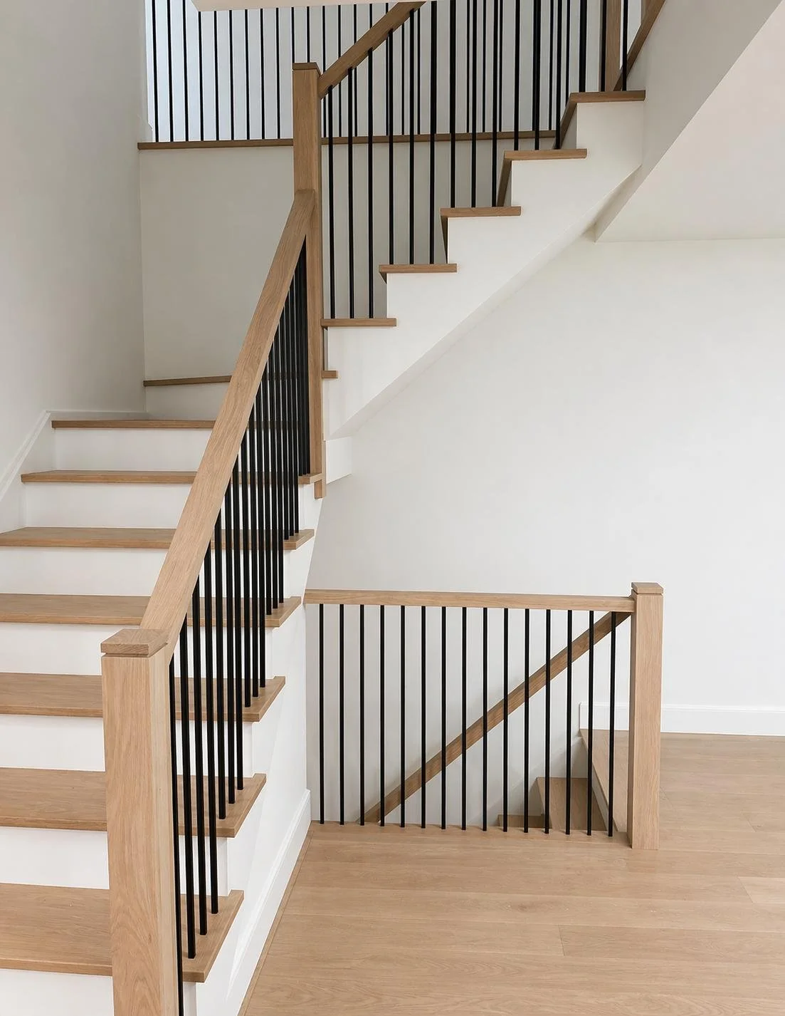 Modern staircase with wood treads, black metal balusters, and wood handrails in a light-colored room.