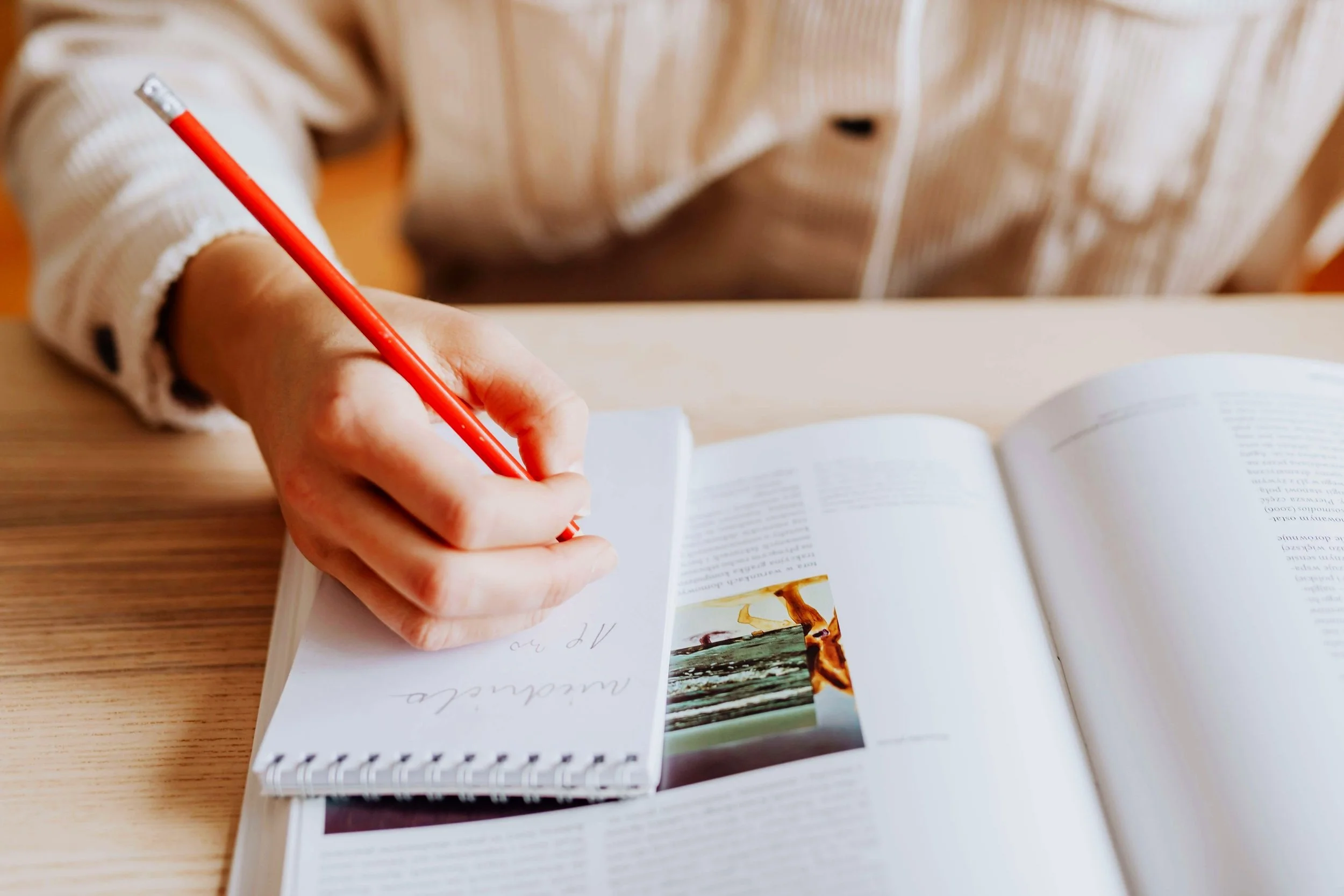 Im Bild zu sehen eine Hand die etwas mit einem orange farbenen Bleistift schreibt