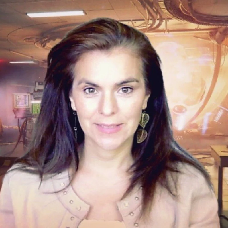 A woman with shoulder-length dark hair, wearing earrings and a beige top, smiling at the camera with a futuristic or sci-fi background featuring a glowing orange light, machinery, and a metallic interior.