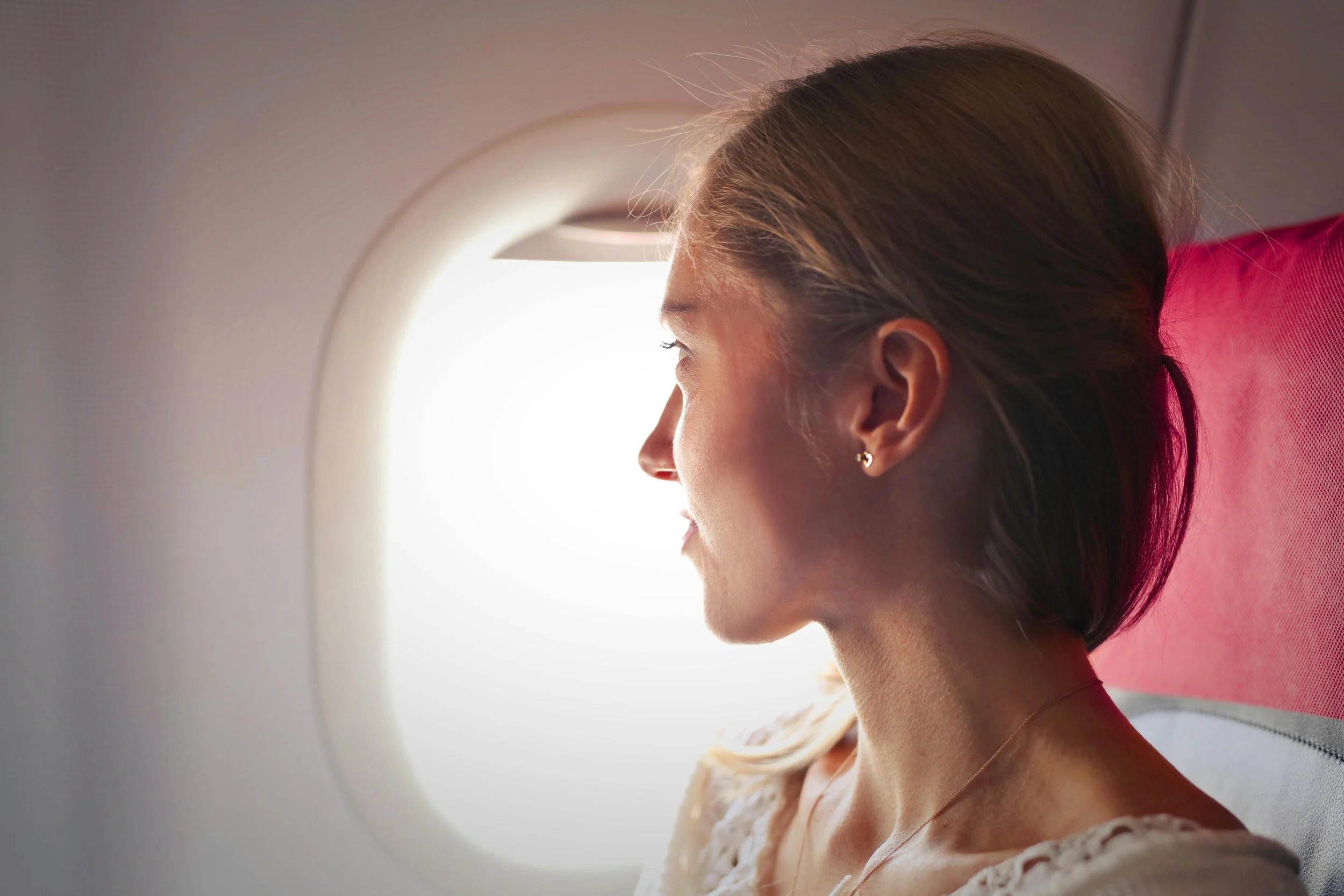 A woman sitting on an airplane seat, looking out of the window.
