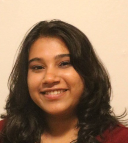A young woman with dark wavy hair smiling at the camera against a plain light-colored background.