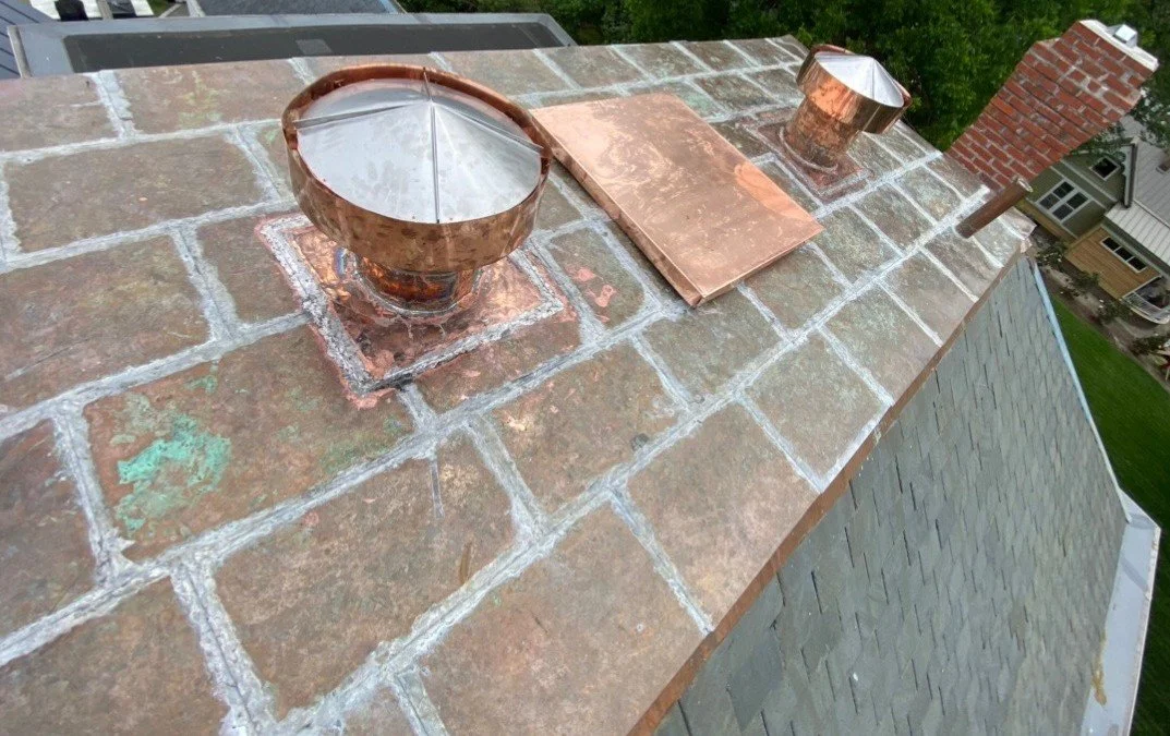 Close-up of a newly installed copper flat seam roof featuring custom-soldered vents and panels with visible soldering joints and a natural patina beginning to form."
