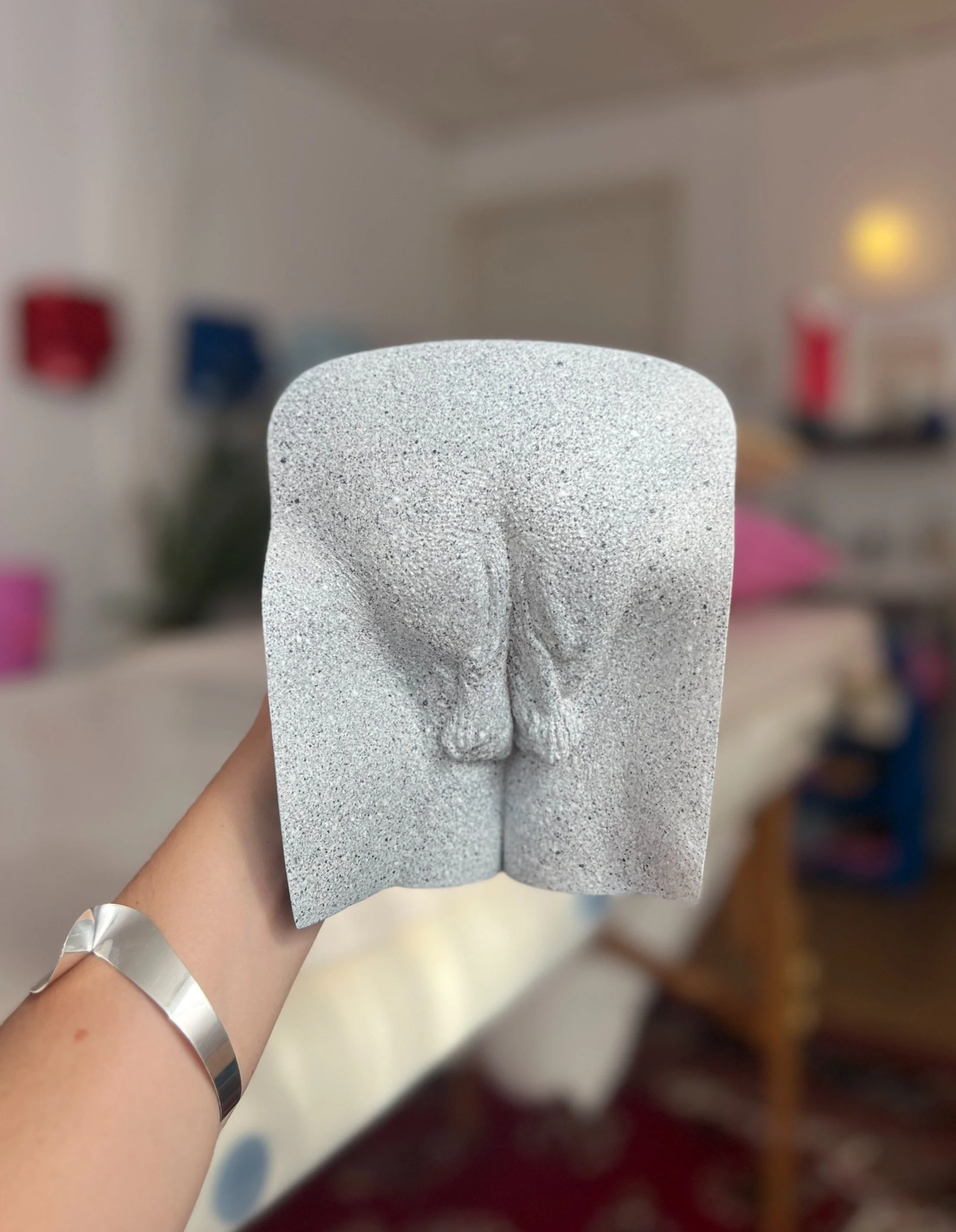 Een hand houdt een betonnen sculptuur van een naakt achterwerk en benen, met een speelse en artistieke uitstraling.