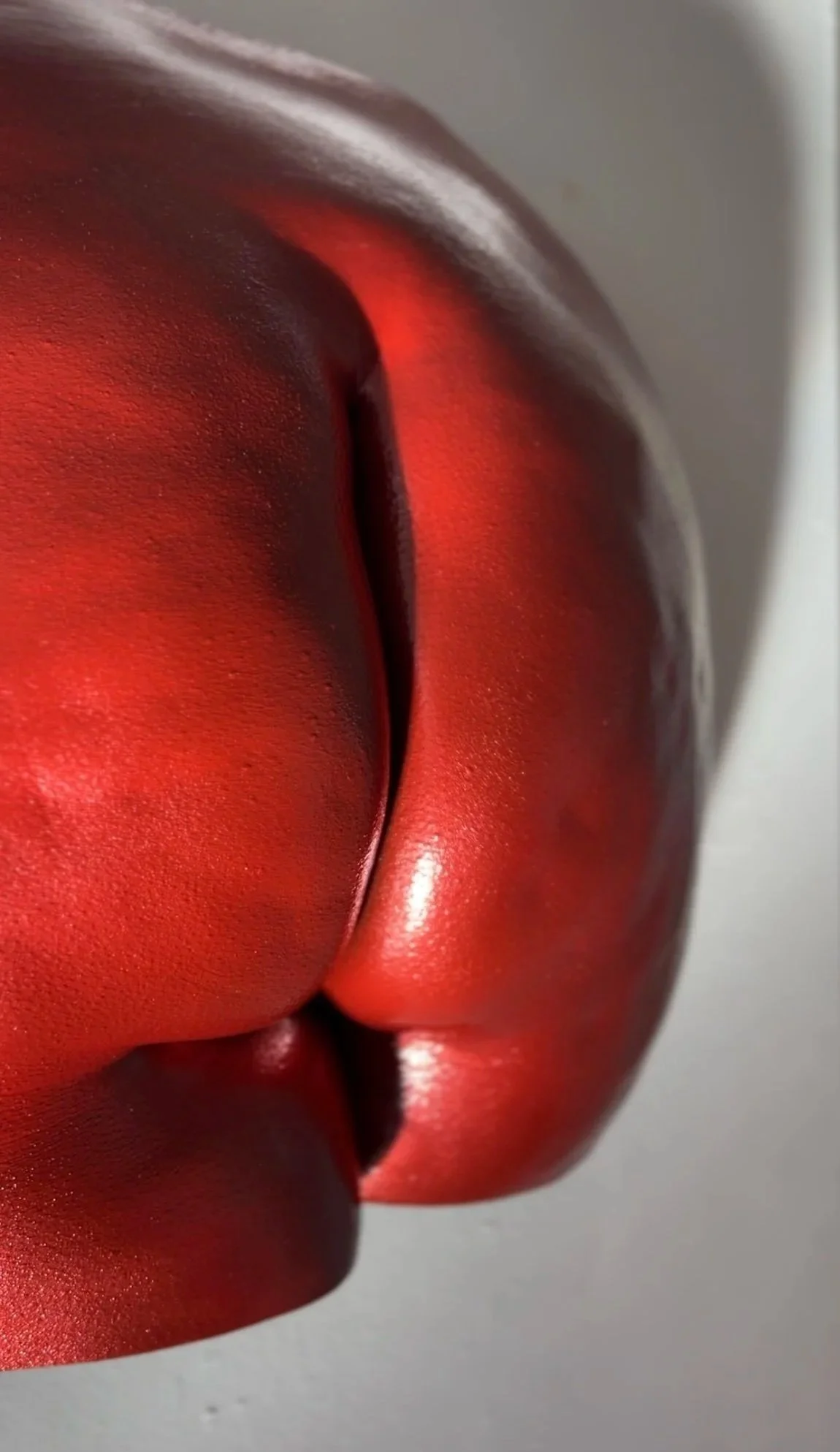 Close-up van metallic rode billensculptuur met zichtbare cellulitis en huidstructuur, handgemaakt van hars, kunstwerk van Venus in Vorm, gefotografeerd in het bodycasting atelier met spotlight die schaduw op de muur creëert.