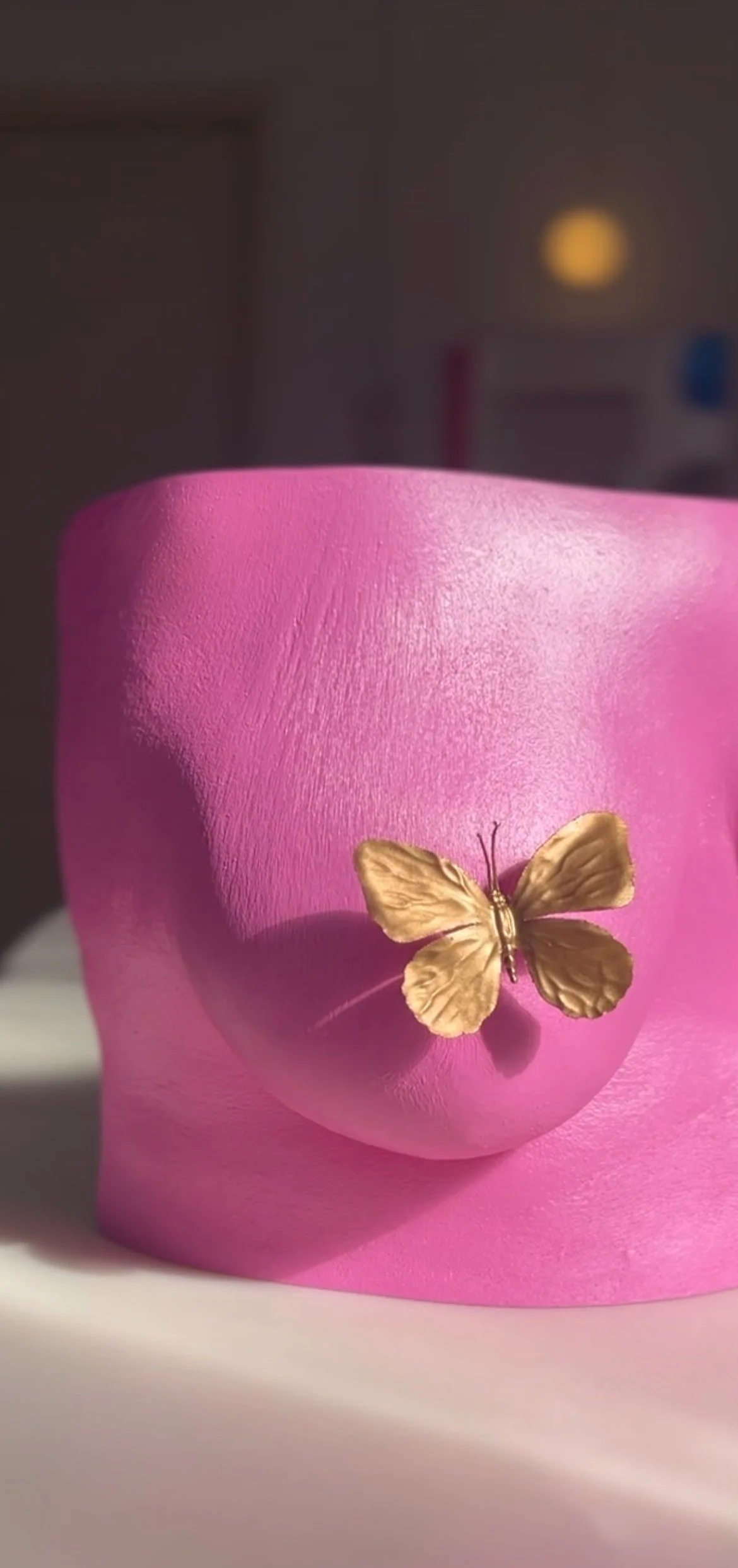 Close-up van body casting sculptuur van roze borst met huidstructuur met gouden vlinder die de tepel bedekt.