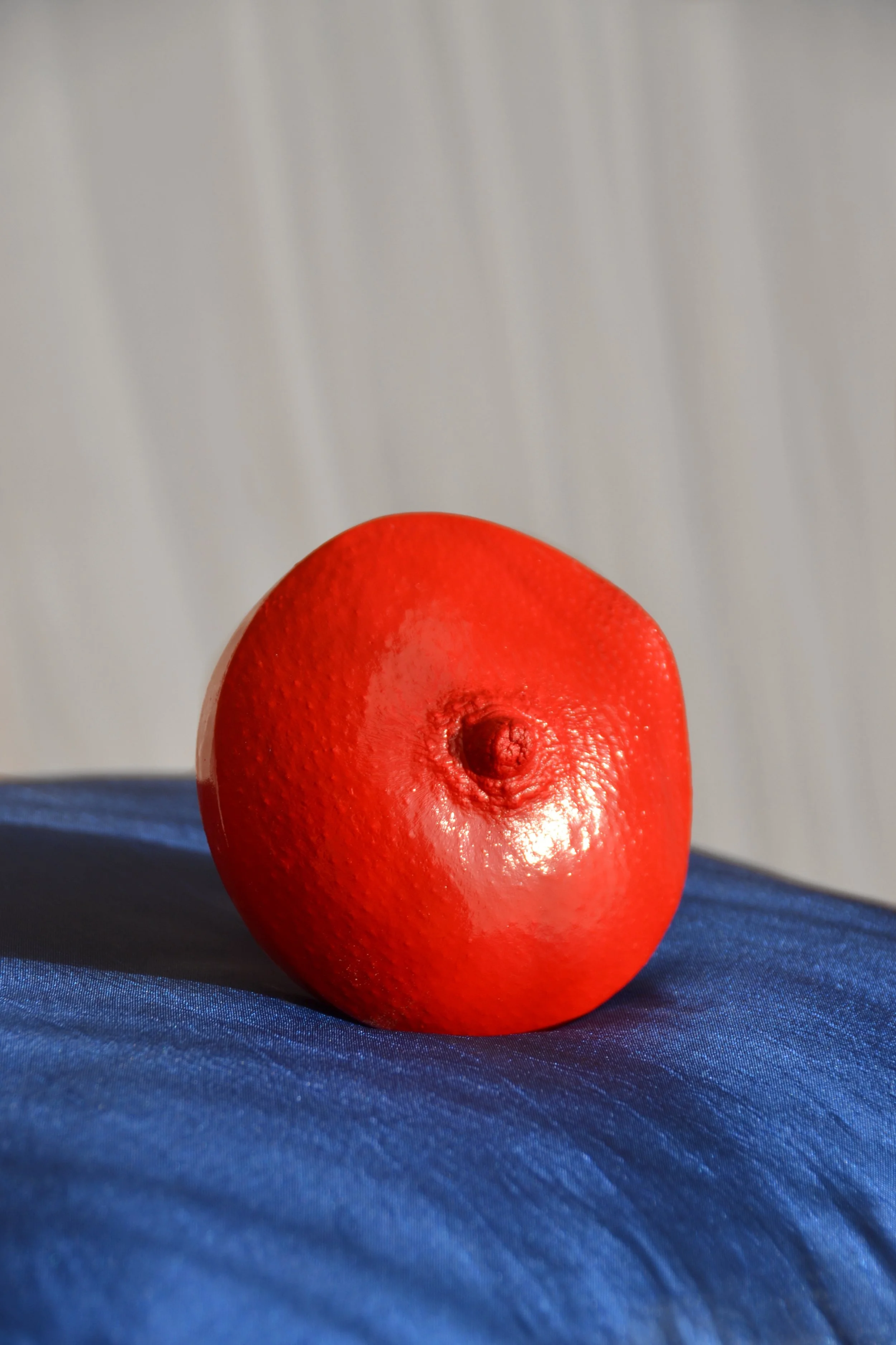 Rood borstbeeld van gips in cirkelvorm met tepel, handgemaakt, geplaatst op glanzend felblauw zijden kussen, kunstwerk van Venus in Vorm, met witte gordijnen op de achtergrond.