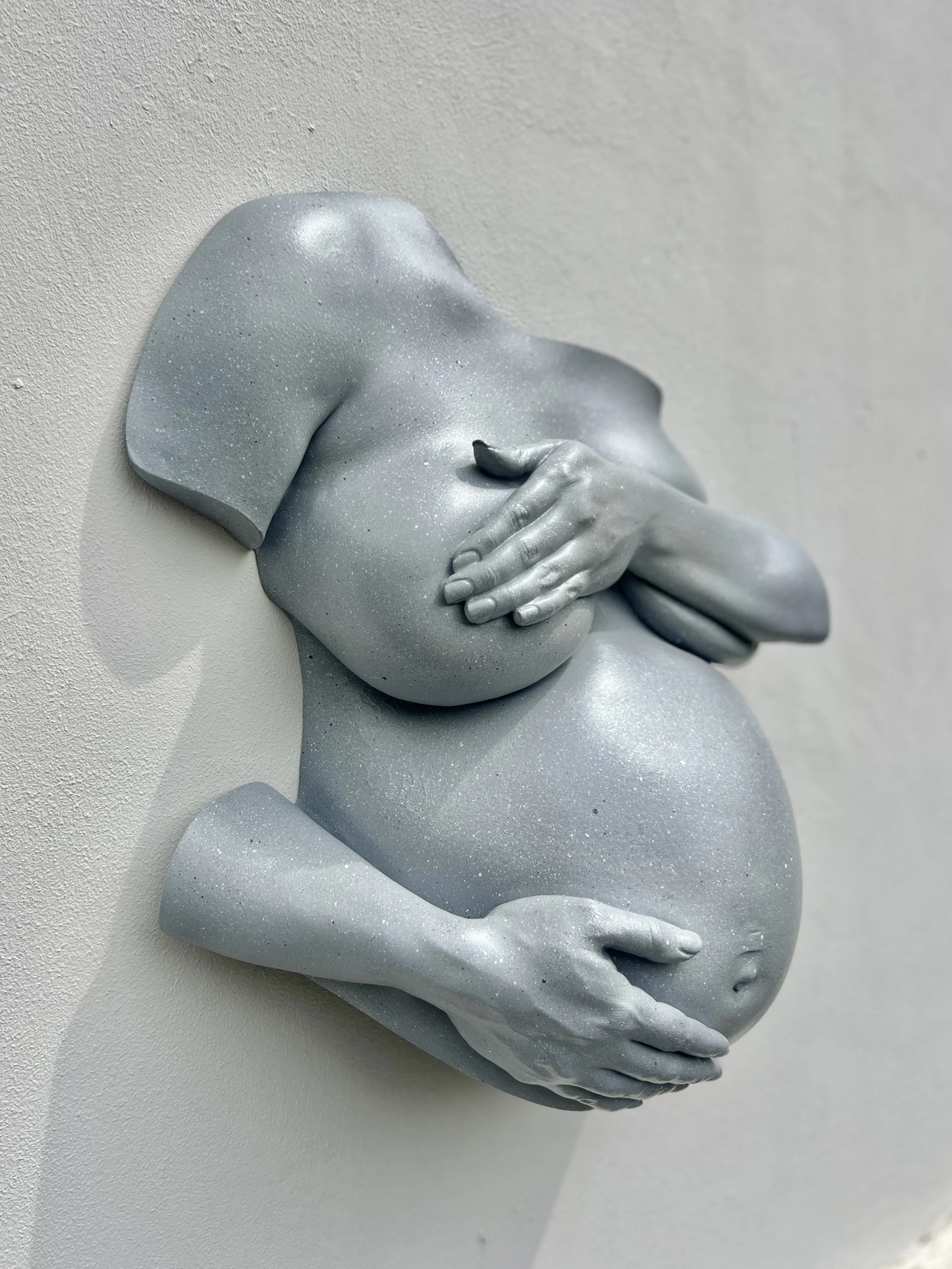 Een sculptuur van een vrouwelijk lichaam met sierlijke handen die een buik vasthouden.