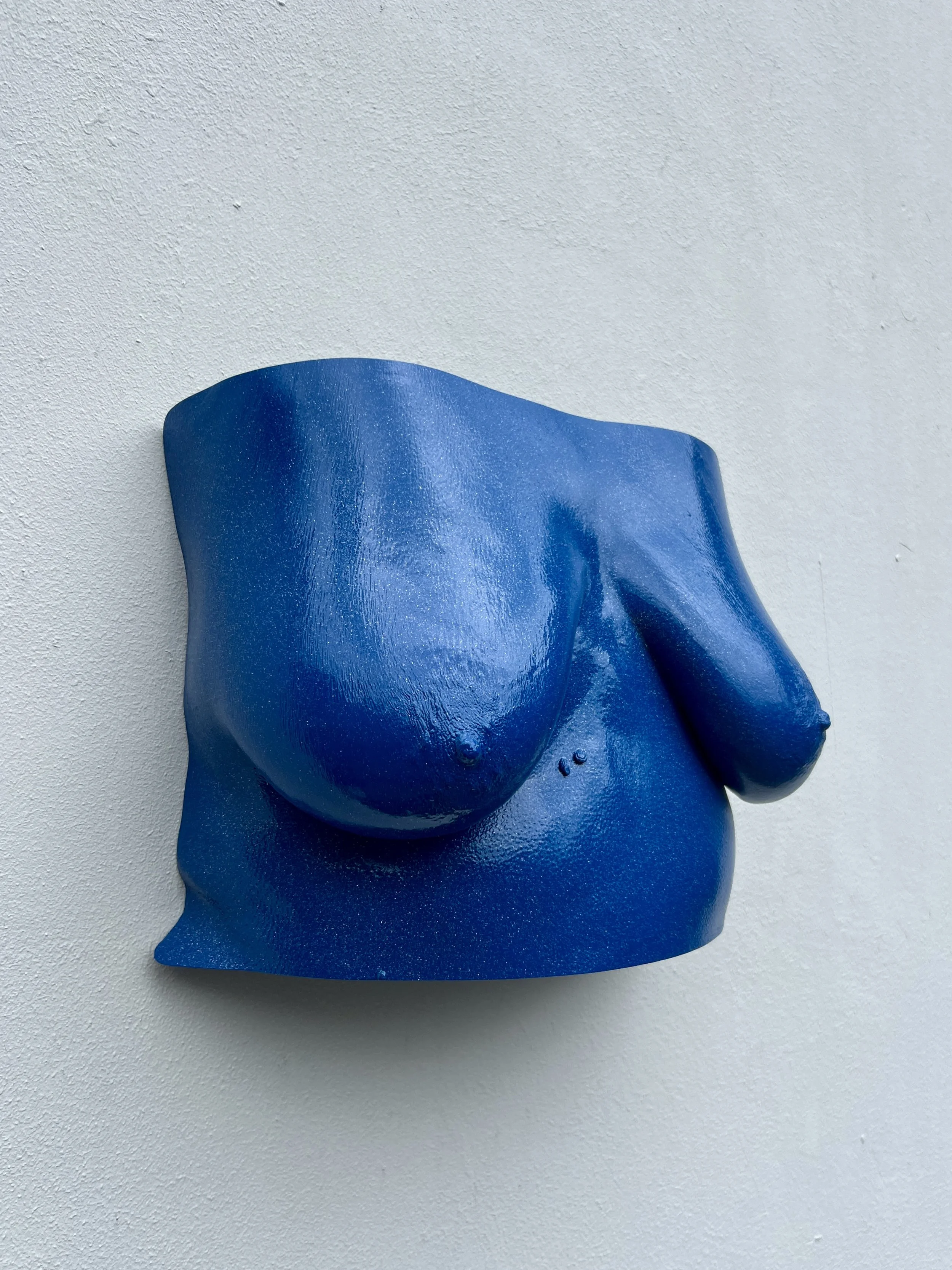 Moderne blauwe sculptuur van een naakte vrouw tegen een witte muur.