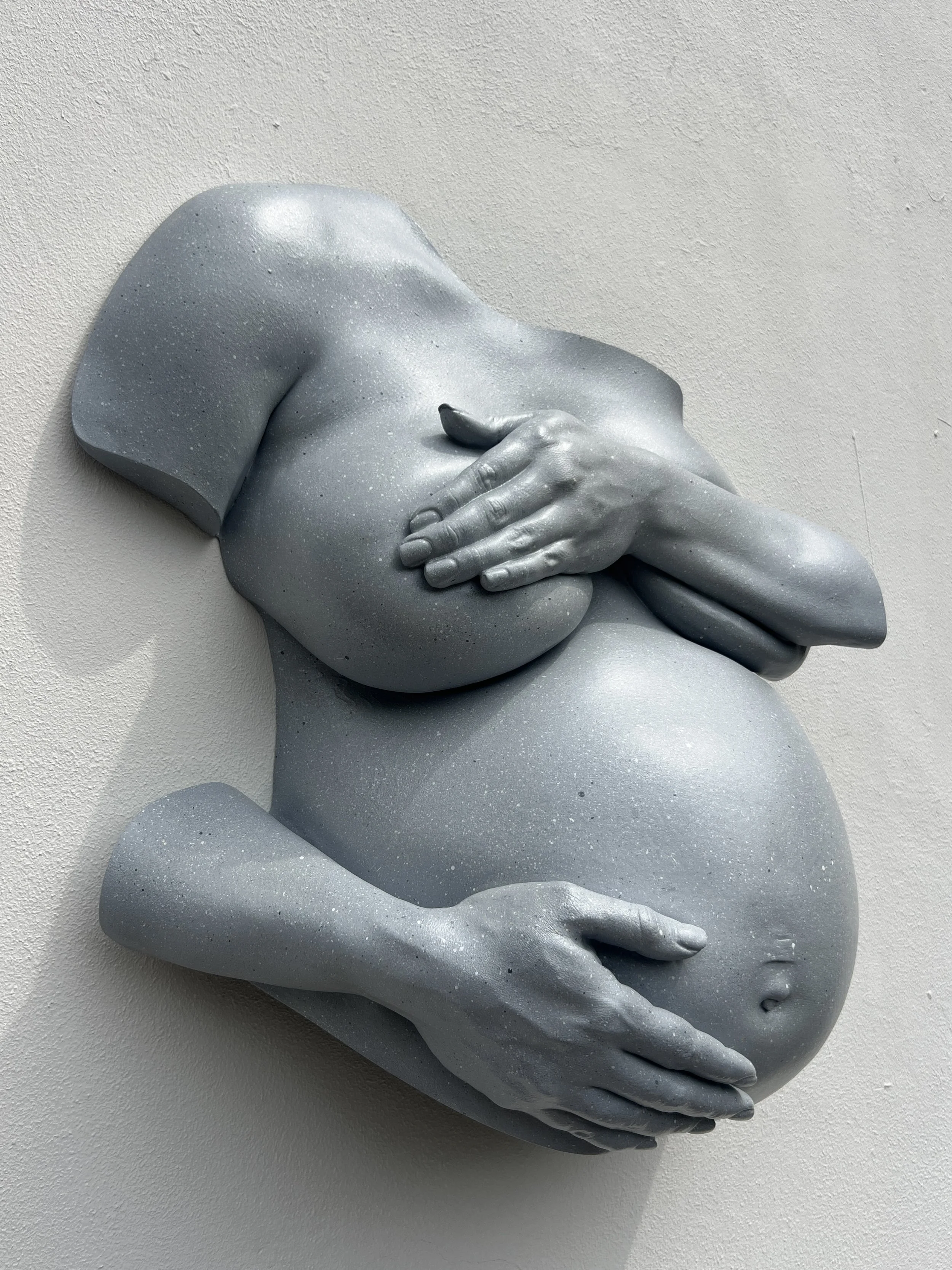 Lichtgrijs beeld van zwangere vrouw met hand en onderarm over borsten en andere hand op buik, handgemaakt van hars met steeneffect afwerking, kunstwerk van Venus in Vorm.