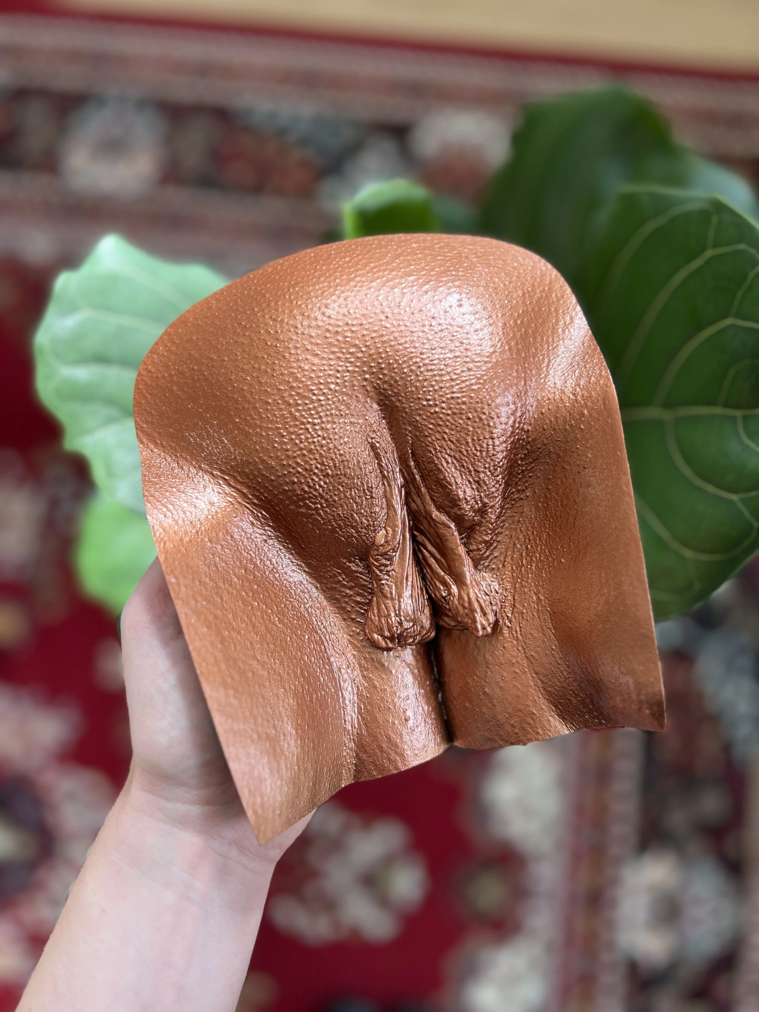 Een hand houdt een brozen vulvasculptuur vast gemaakt via body casting, gemaakt van hars, gefotografeerd in atelier Venus in Vorm.