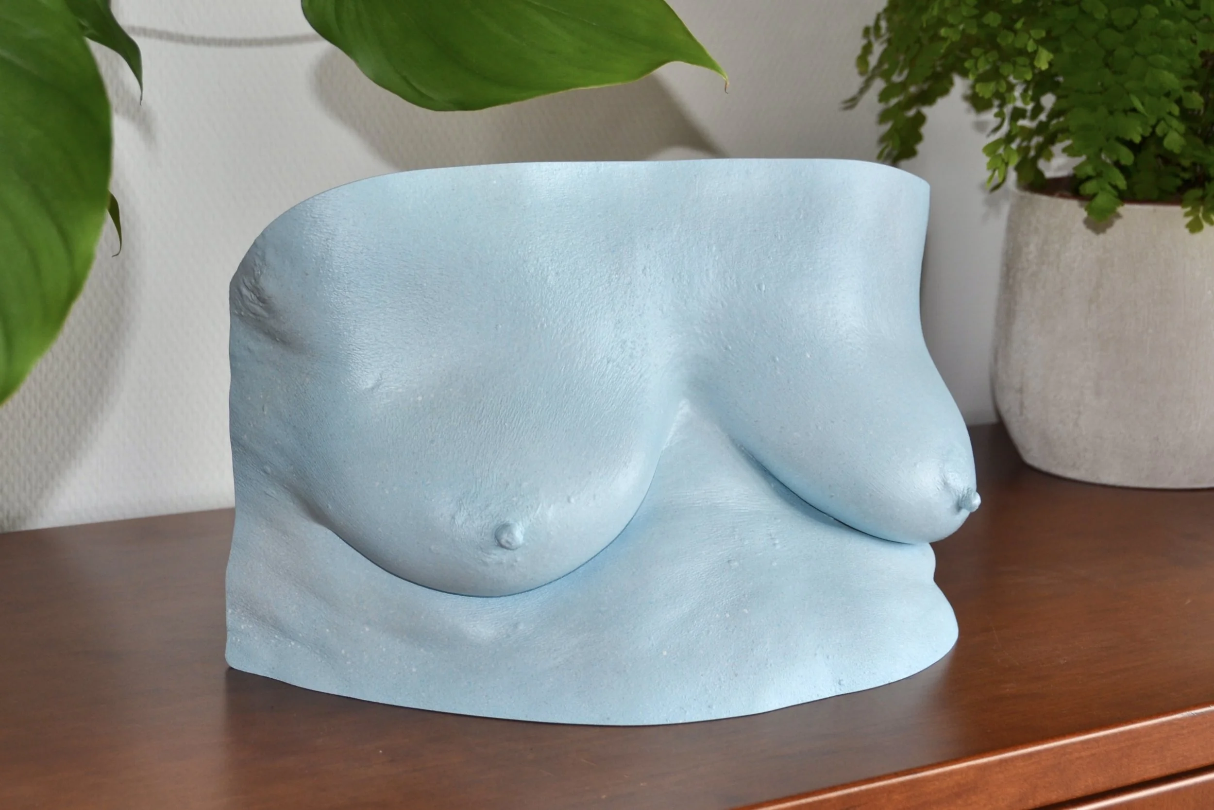 Lichtblauwe bodycasting borstsculptuur met steeneffect afwerking, handgemaakt van hars, kunstwerk van Venus in Vorm, gefotografeerd in interieur op houten kast met planten op de achtergrond