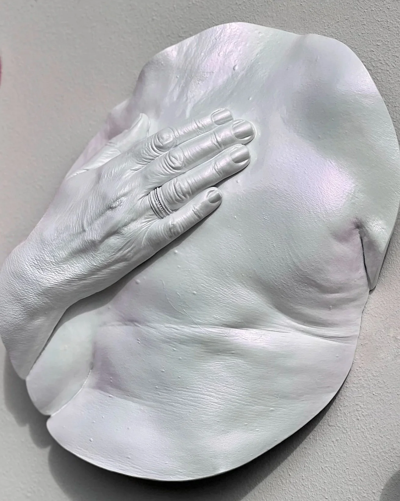 Close-up van witte borstsculptuur met parelmoerroze glans van vrouw na borstamputatie, handgemaakt van hars, details van hand, ring, litteken en vlindertattoo zichtbaar, onderdeel van drieluik over borstzelfonderzoek, kunstwerk van Venus in Vorm.