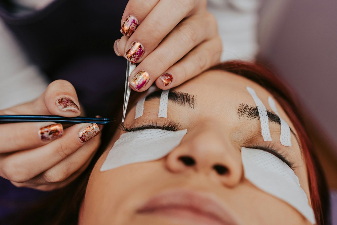 Close-up of lash extension application with eye pads and tweezers, highlighting detailed beauty service