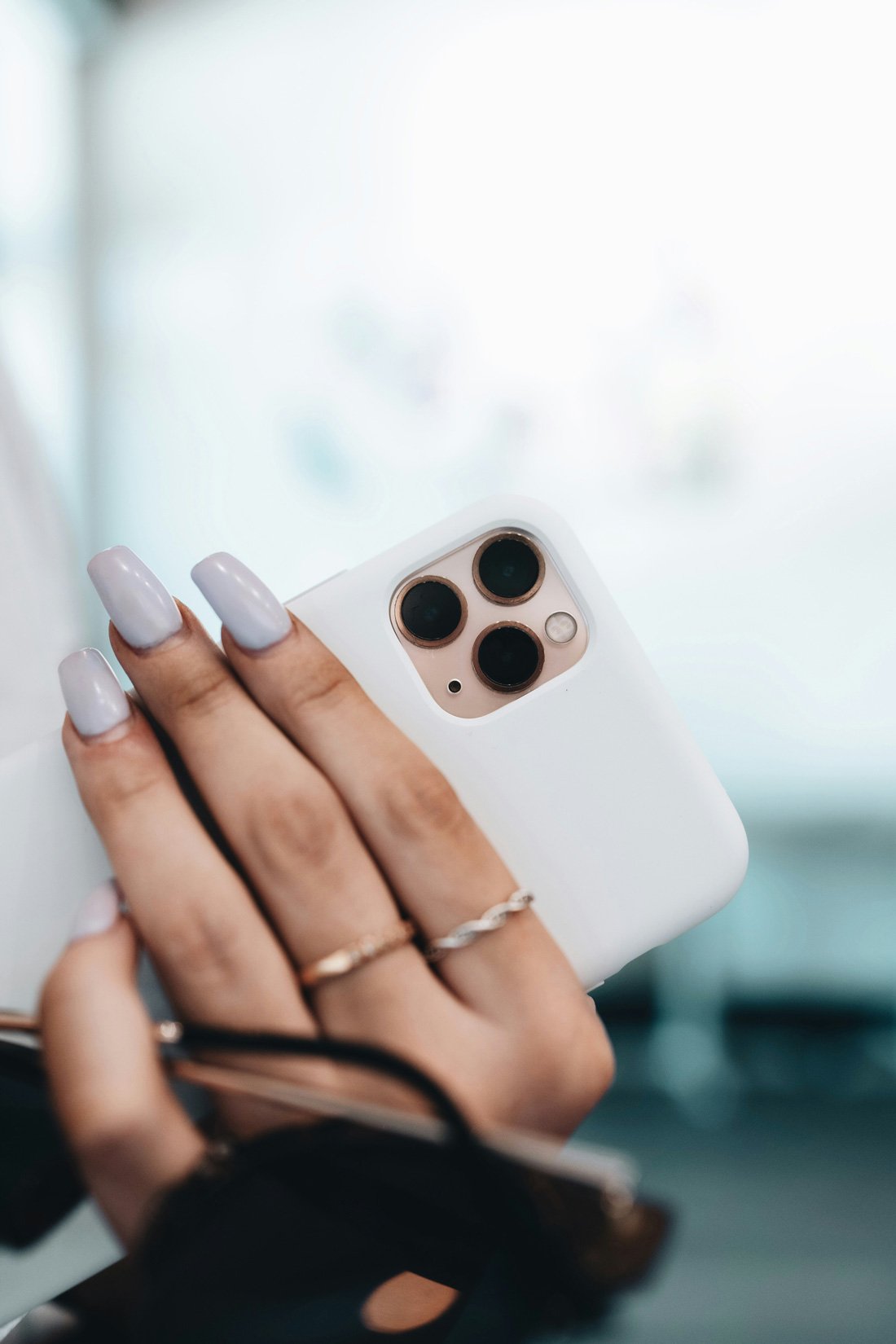 light lavender manicure with long square nails, holding smartphone with white case and gold rings