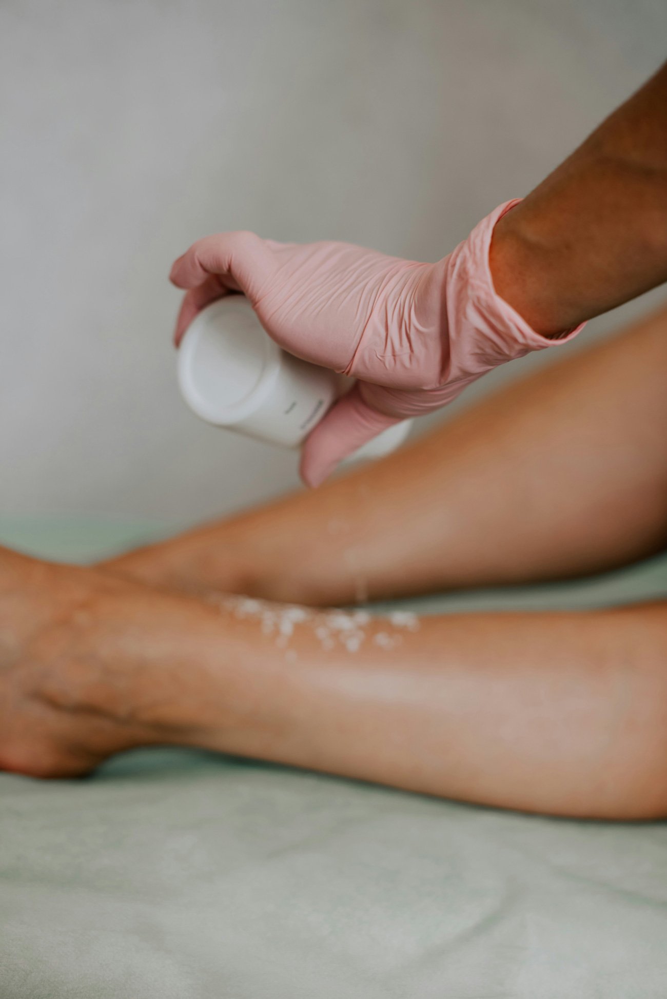 Close-up of gloved hand applying powder on lower leg as part of professional waxing prep